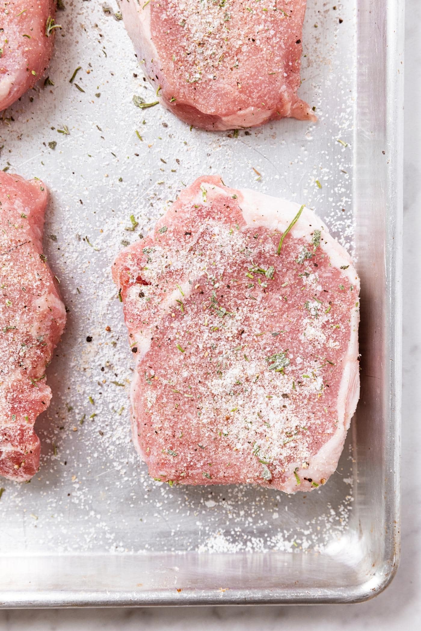 Raw pork chops sitting on metal baking dish with dry brine made from salt sprinkled all over the top.