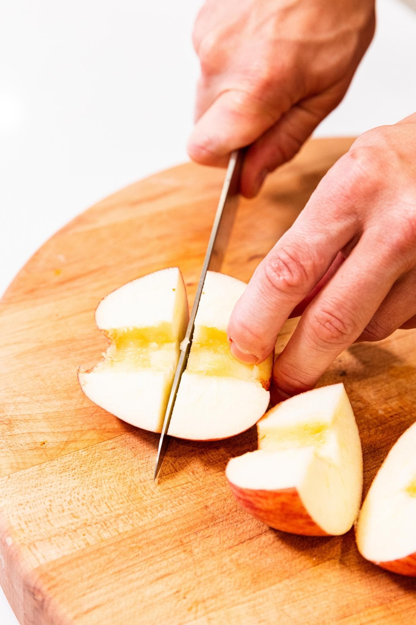 Two hands slicing up apples on wood cutting board.