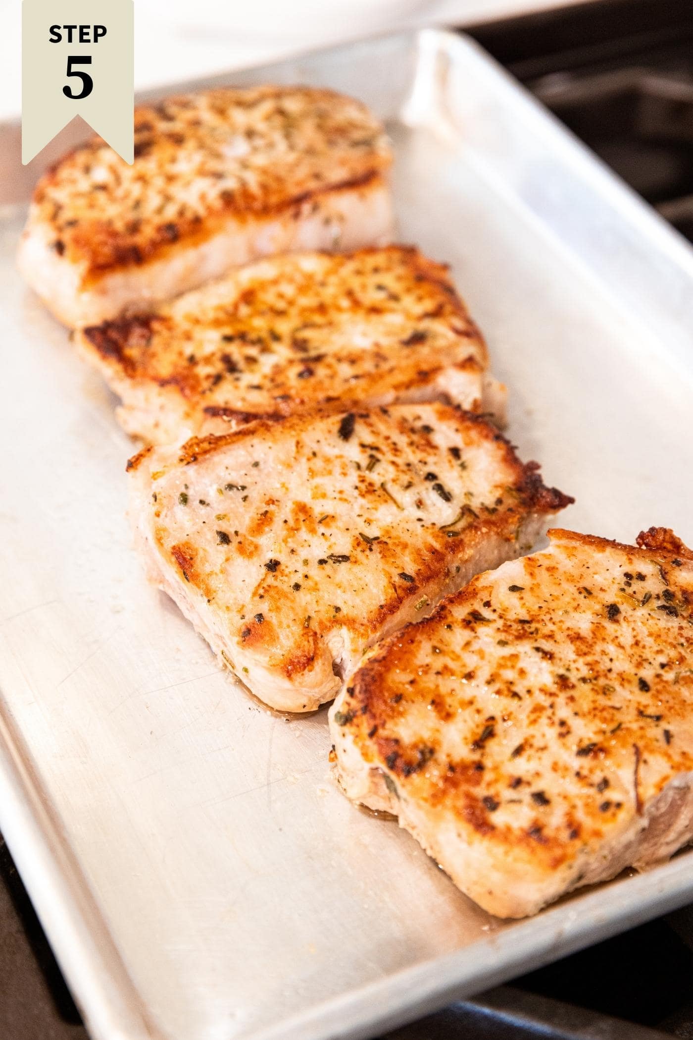 Browned and fully cooked pork chops sitting on metal baking dish on stovetop after being removed from skillet.