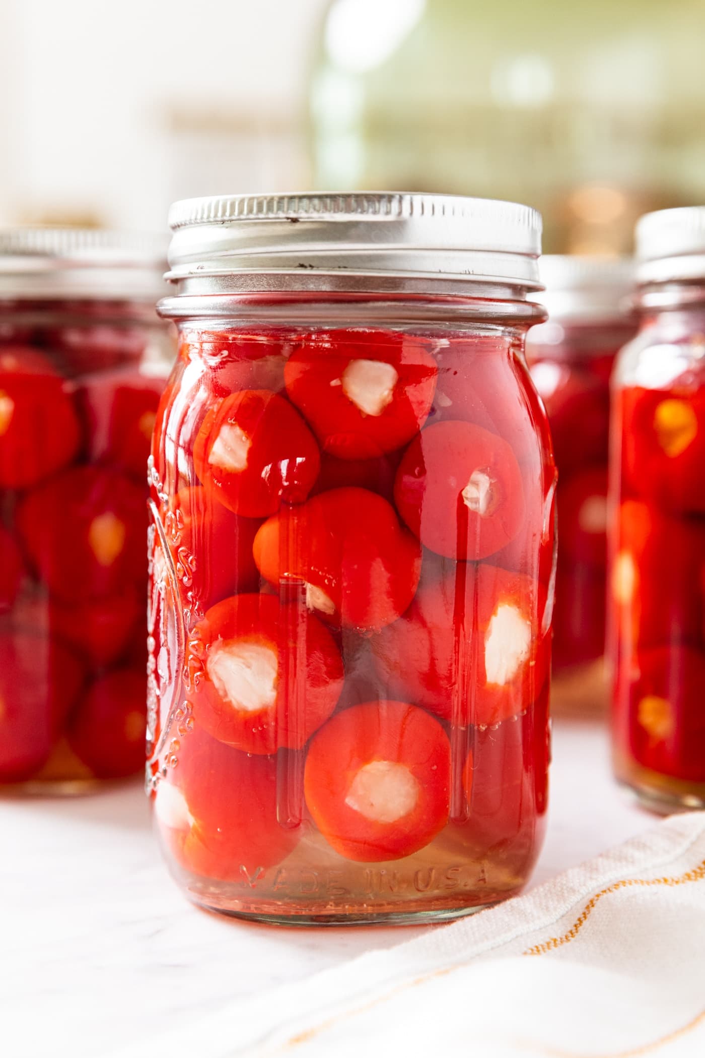 Glass canning jar filled with stuffed pickled peppers with more canning jars also filled in background all on marble surface.