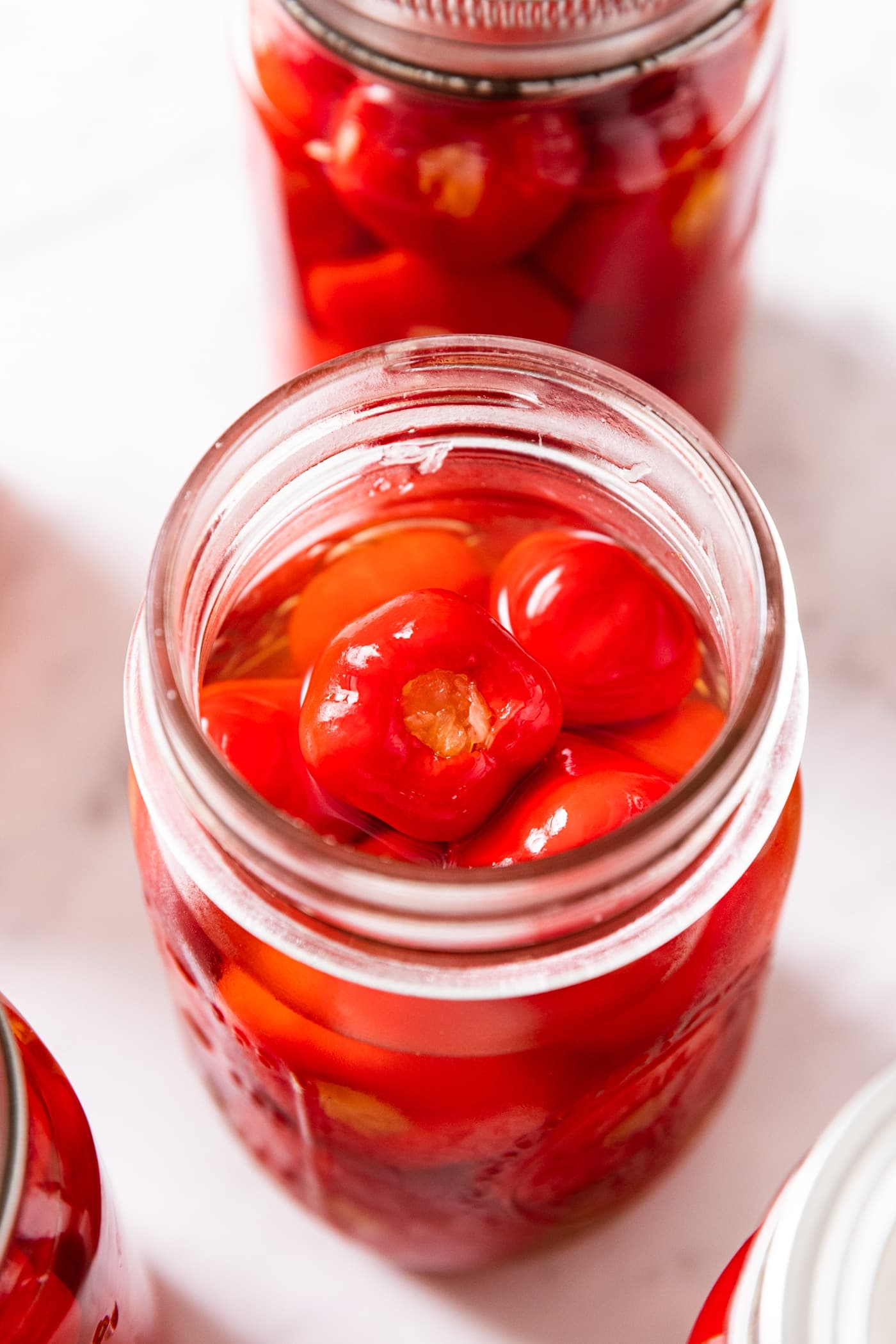 Glass canning jar filled with red colored miniature stuffed peppers with jar open showing inner contents including the brine.