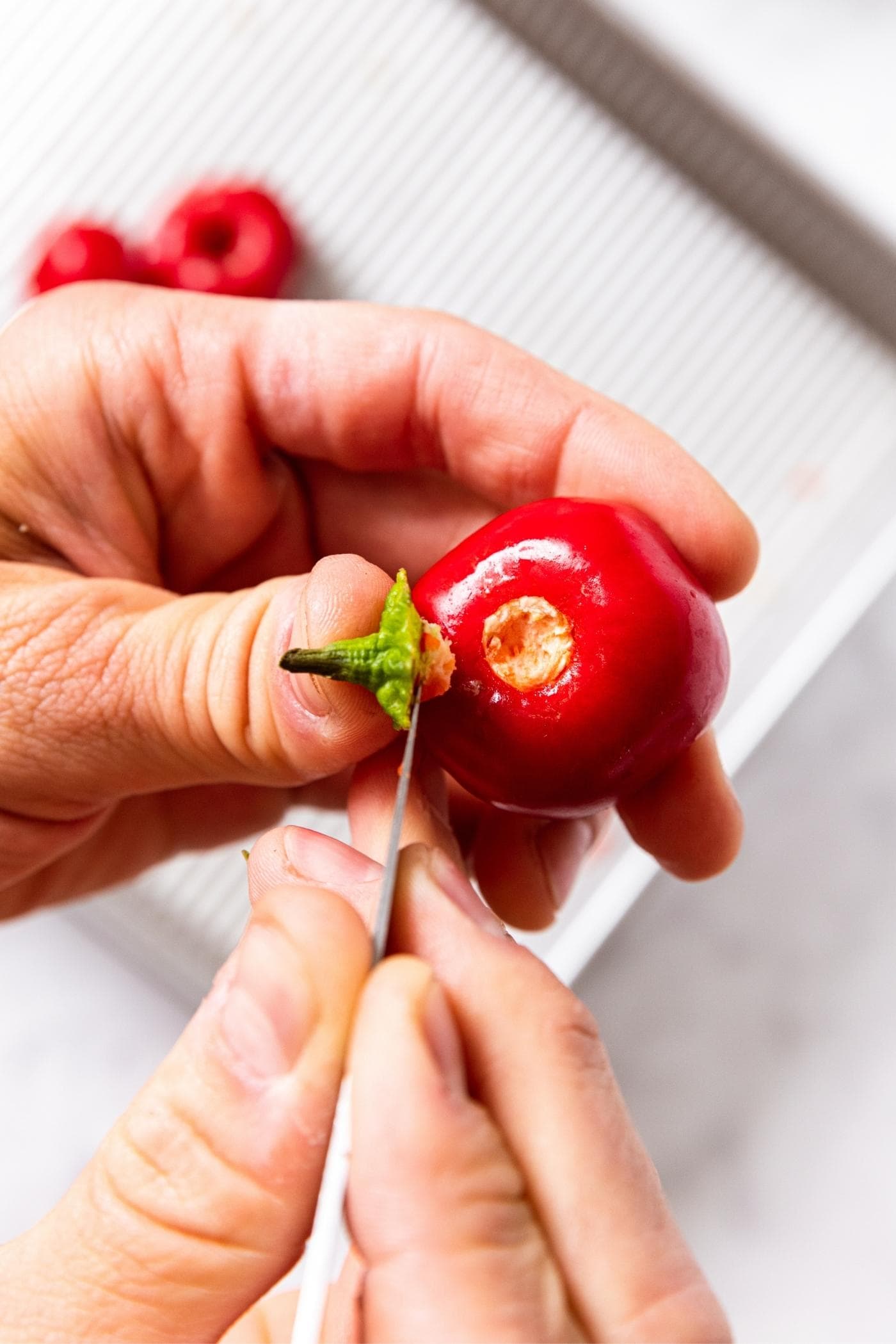 Hands using knife to cut off the stem of a small miniature red pepper.