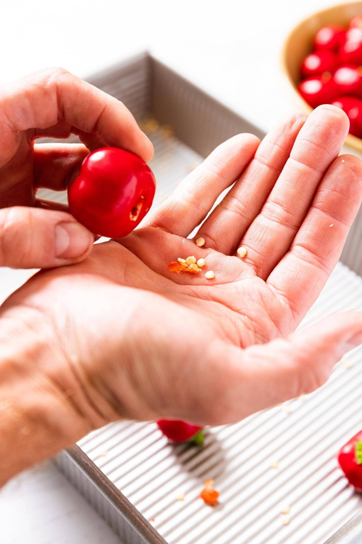 Hand dumping out the seeds from the inside of a small red sweet pepper with more peppers in background.