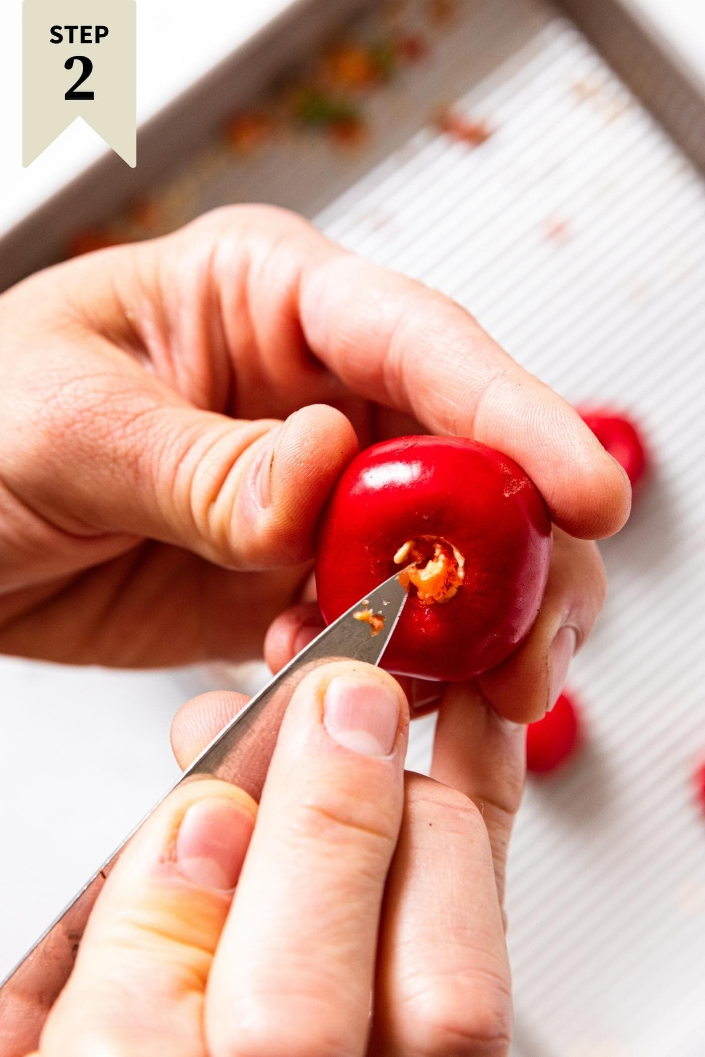 Hand using a knife to scoop out the insides of a small red pepper including the pith.