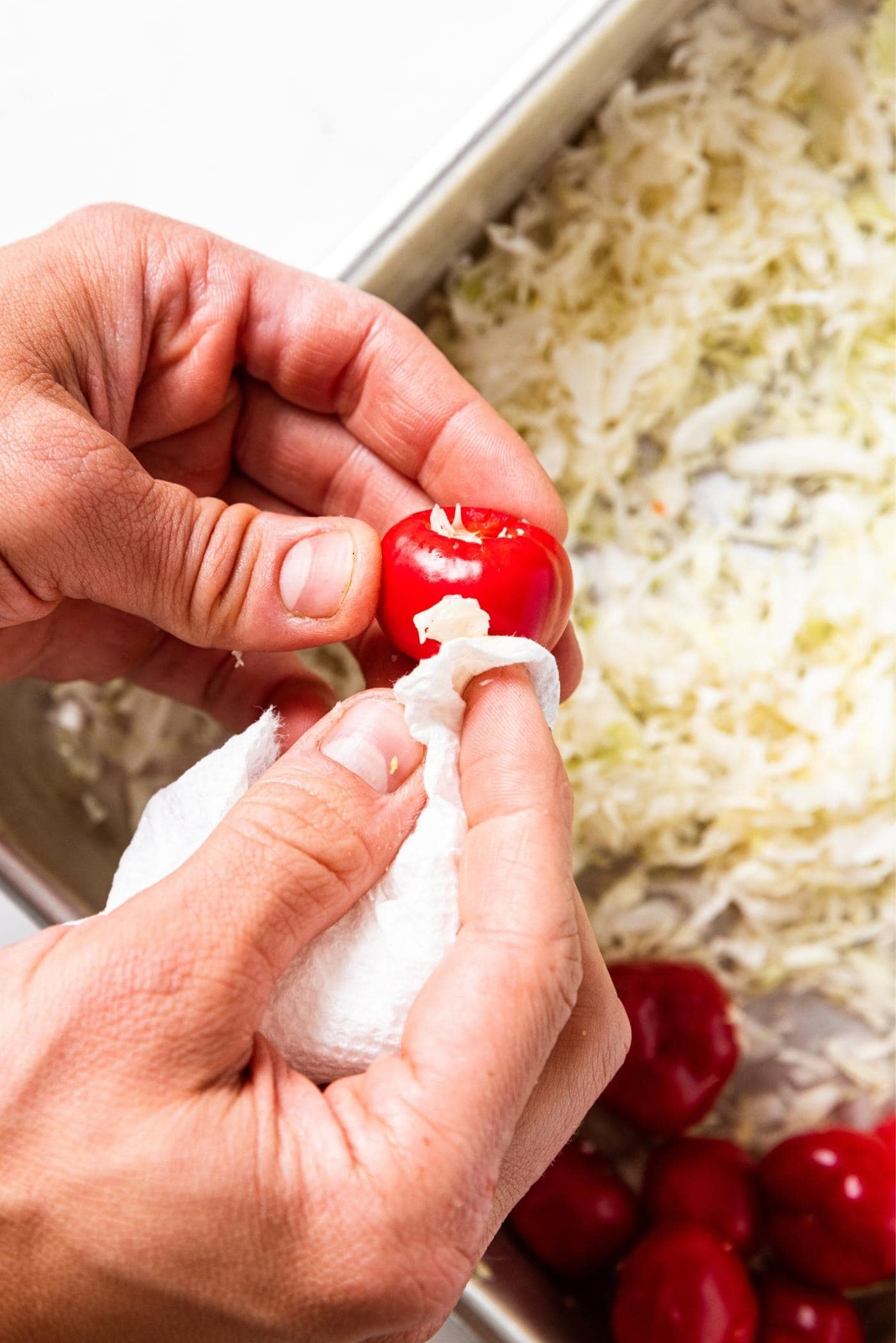 Two hands holding a small red miniature pepper using a paper towel to wipe off any excess cabbage from outside surface.