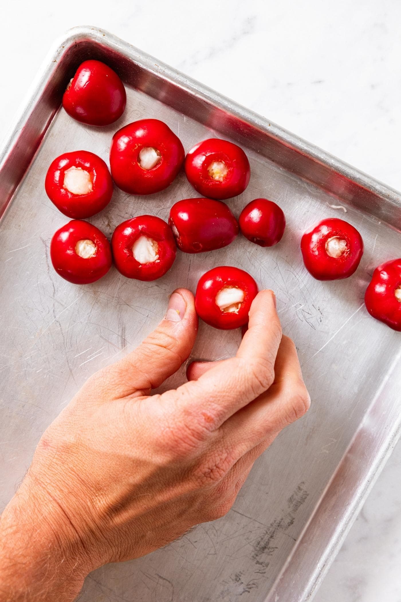 Hand placing red sweet pepper stuffed with raw cabbage on metal cooking sheet.