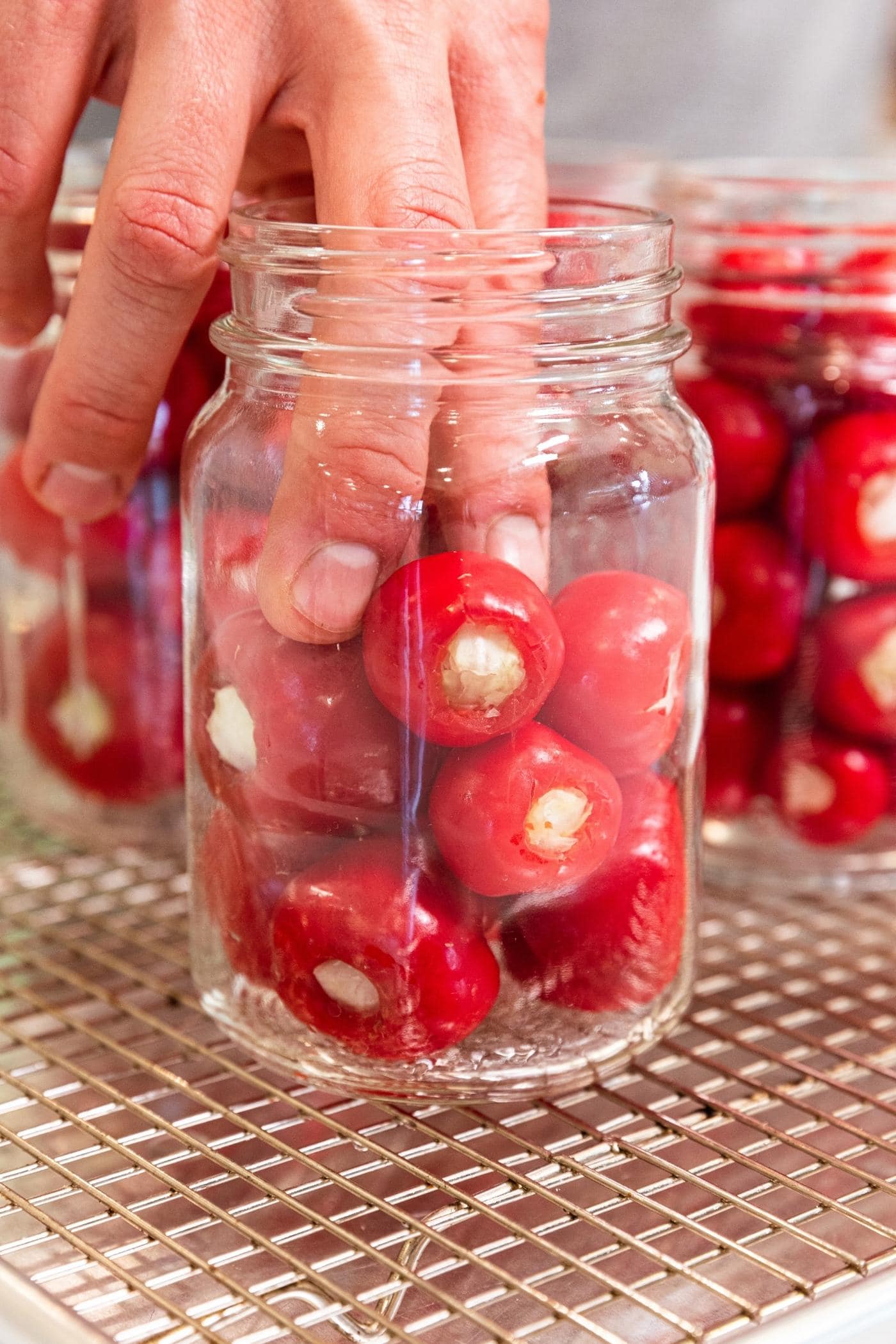 Hand using fingers to place stuffed red peppers in glass canning jar before pouring on the brine.