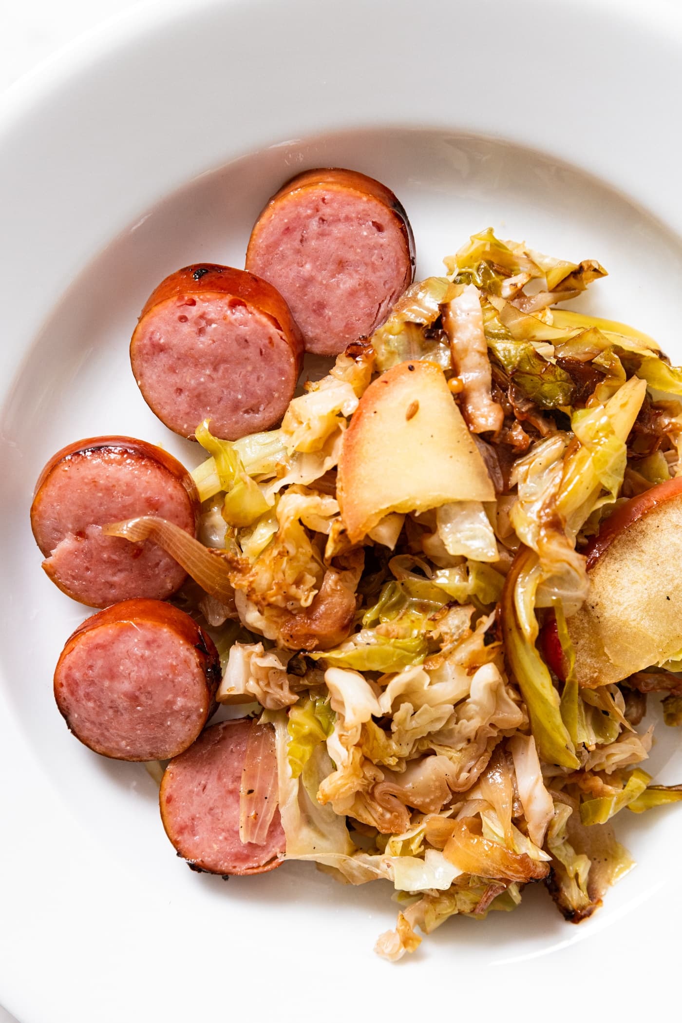 White plate with slices of cooked kielbasa with a helping of cabbage and apple on side.