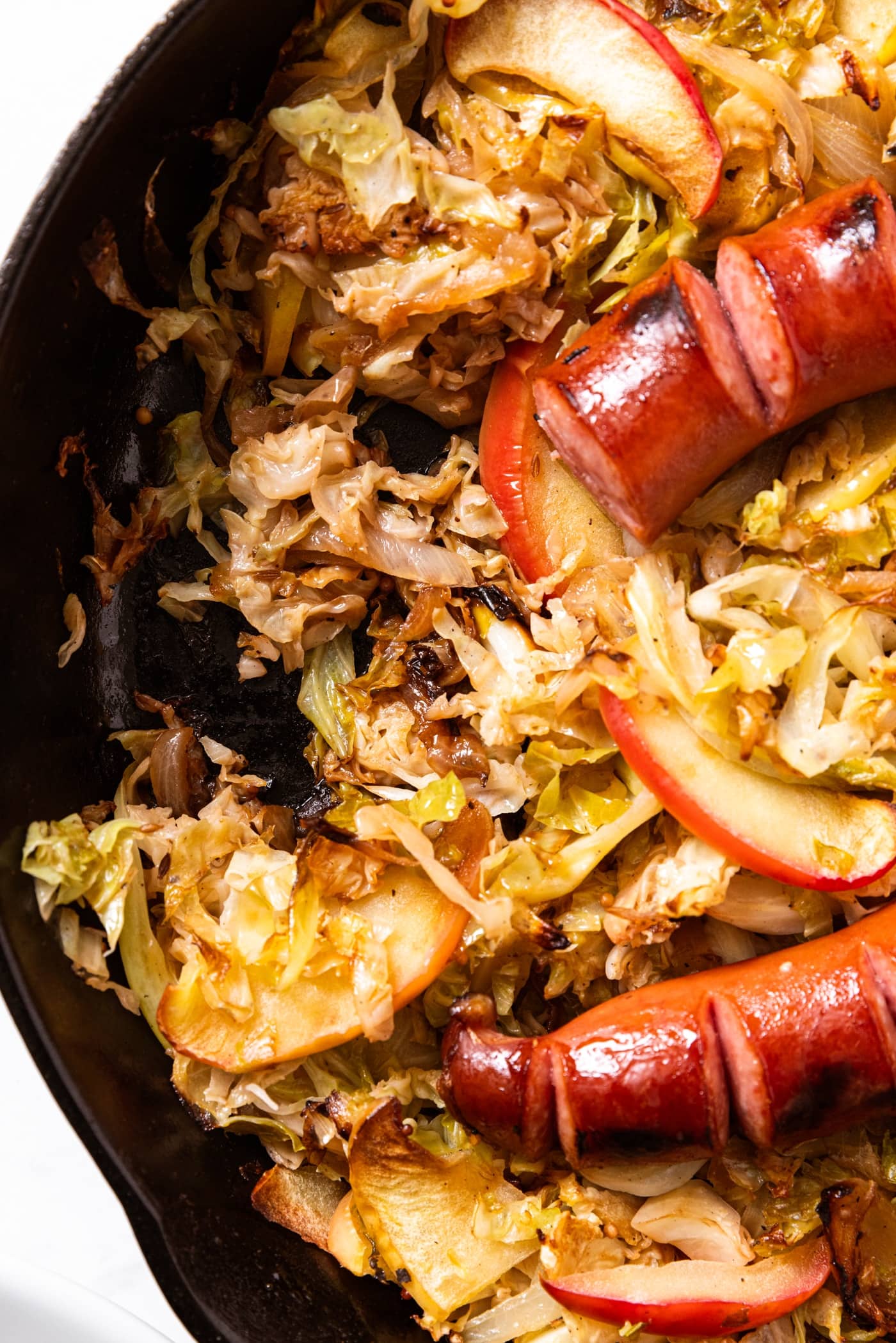 Black cast iron skillet with cooked cabbage and slices of apple topped with browned kielbasa.