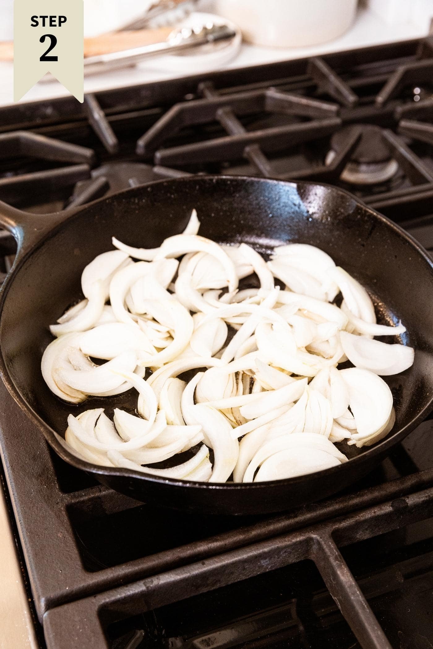 Black cast iron skillet sitting on stovetop with slices of onion about to brown on heat. 