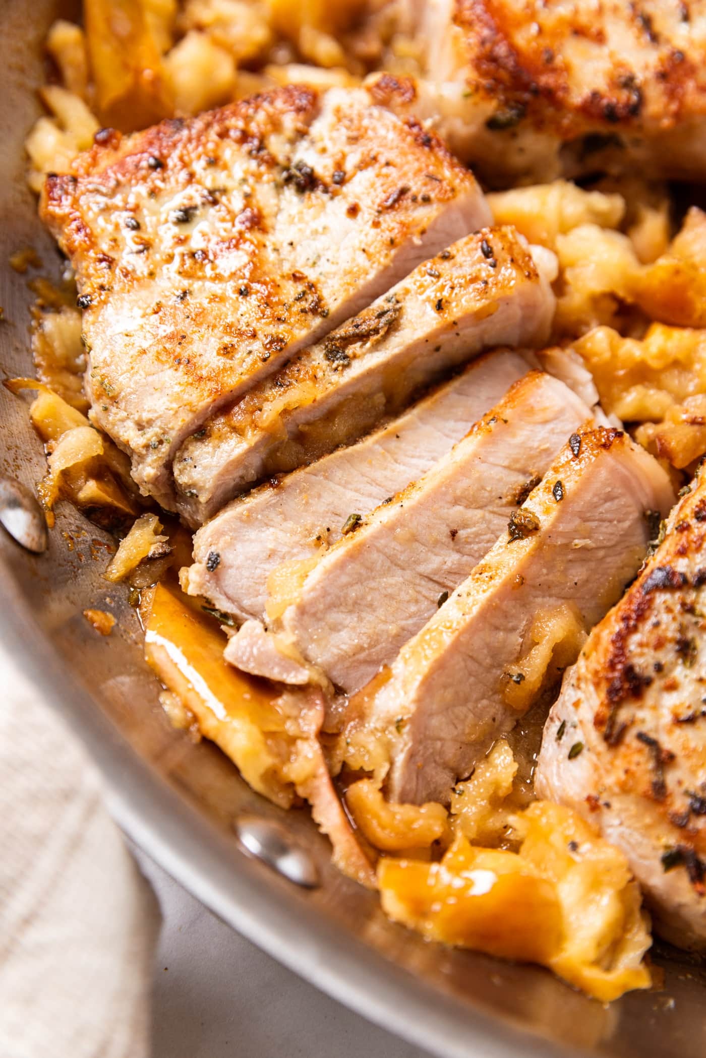 Metal skillet filled with smashed apples and browned pork chops with part of one sliced into slices.