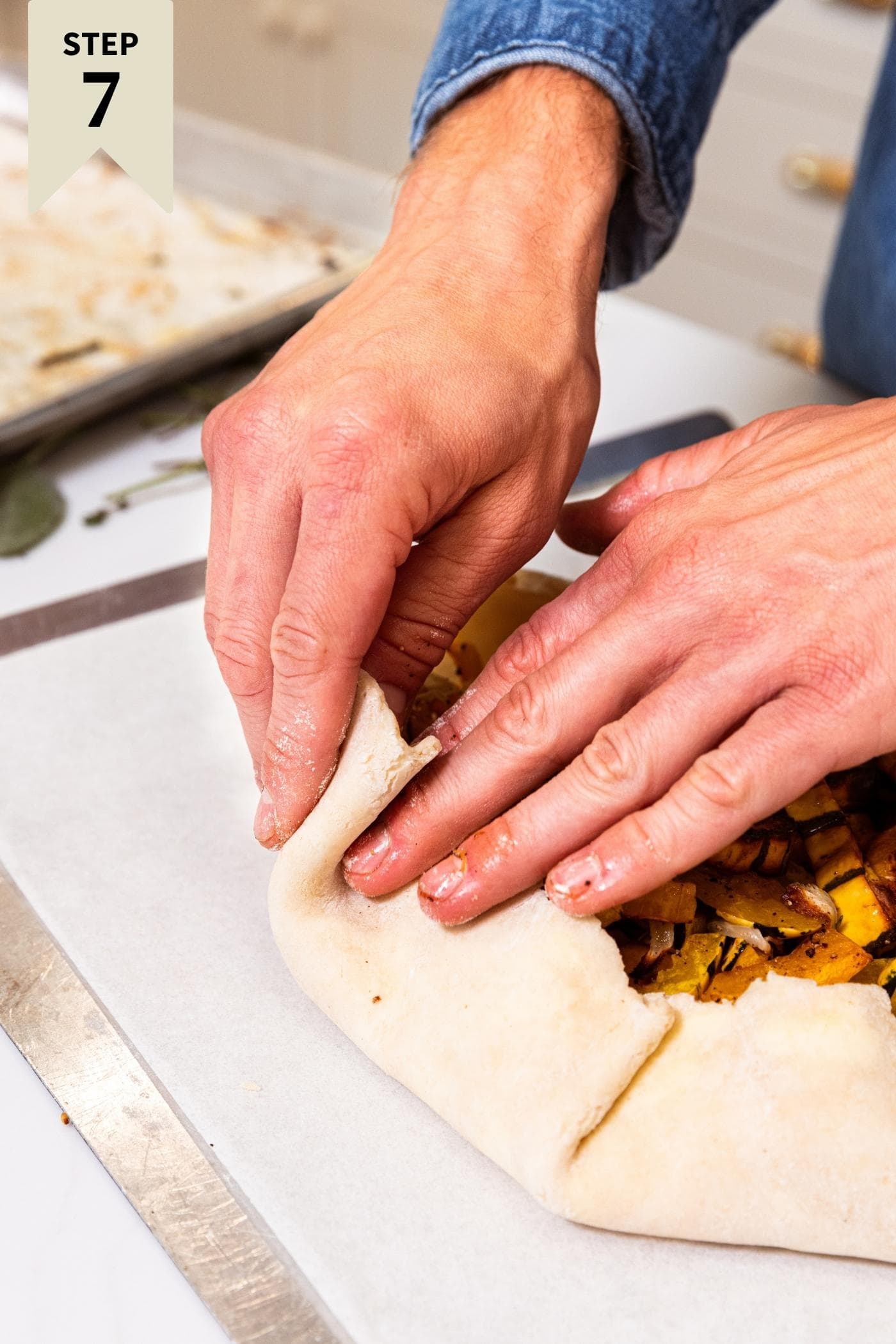 Two hands pushing up the sides of dough to form a galette on a parchment-lined baking sheet.