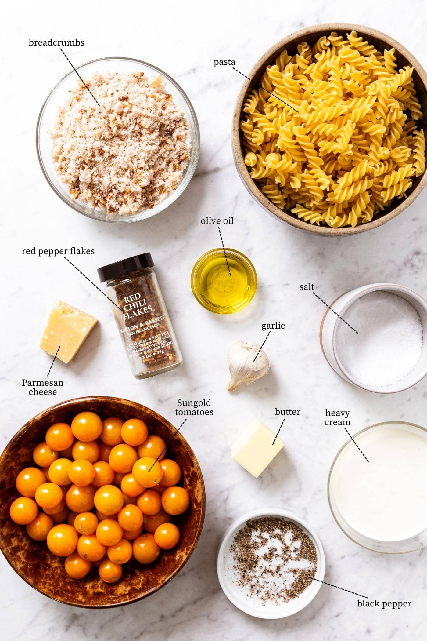 Marble surface filled with all of the ingredients needed to make a Sungold tomato pasta dish including tomatoes, butter, cheese, breadcrumbs, pasta, and more.