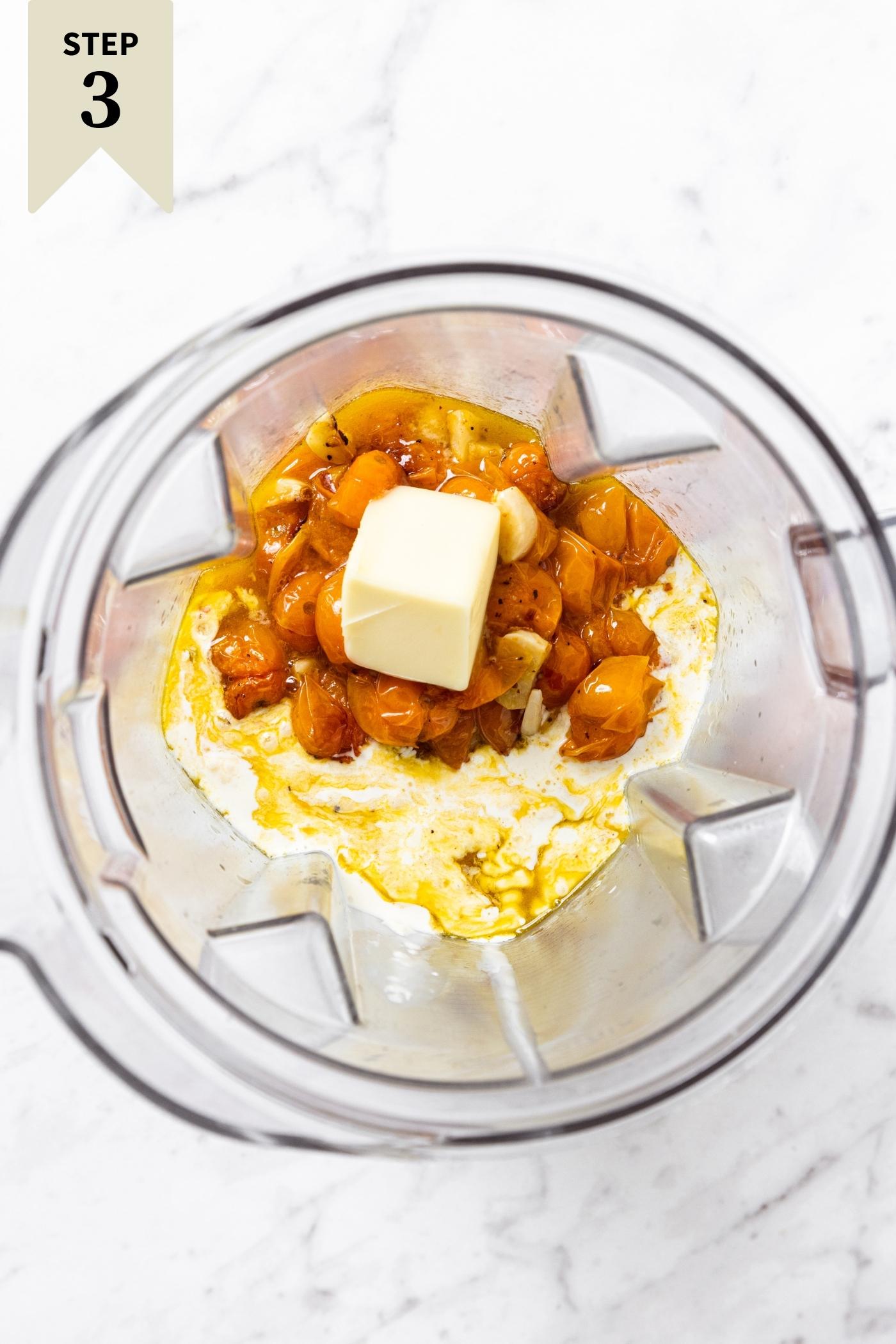 Clear blender container filled with unblended roasted tomatoes, butter, and cream all sitting on marble surface.