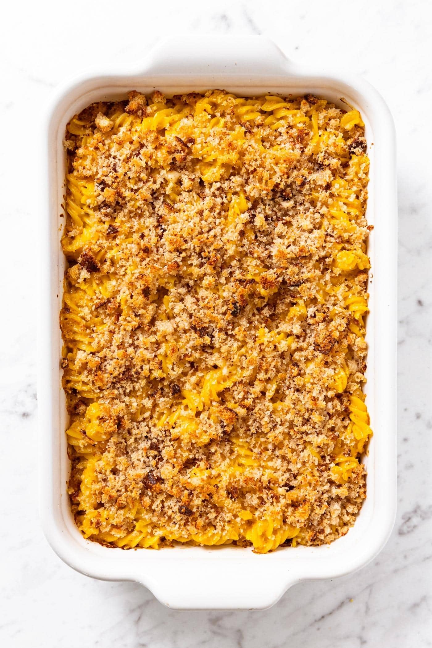 Baked rotini pasta with crispy breadcrumb topping after coming out of the oven sitting on marble surface.