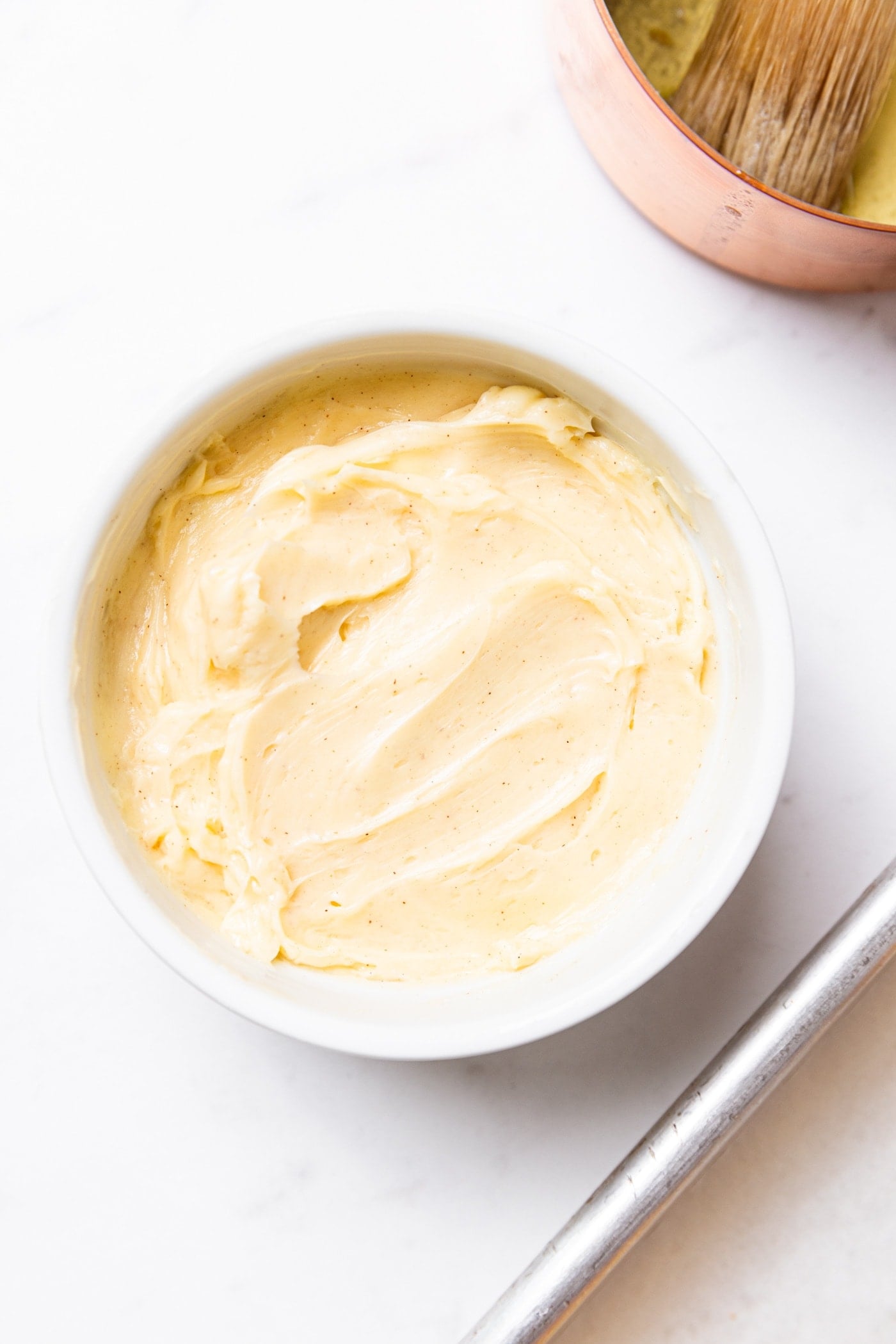 Small circular white bowl sitting on marble surface filled with cinnamon honey butter.