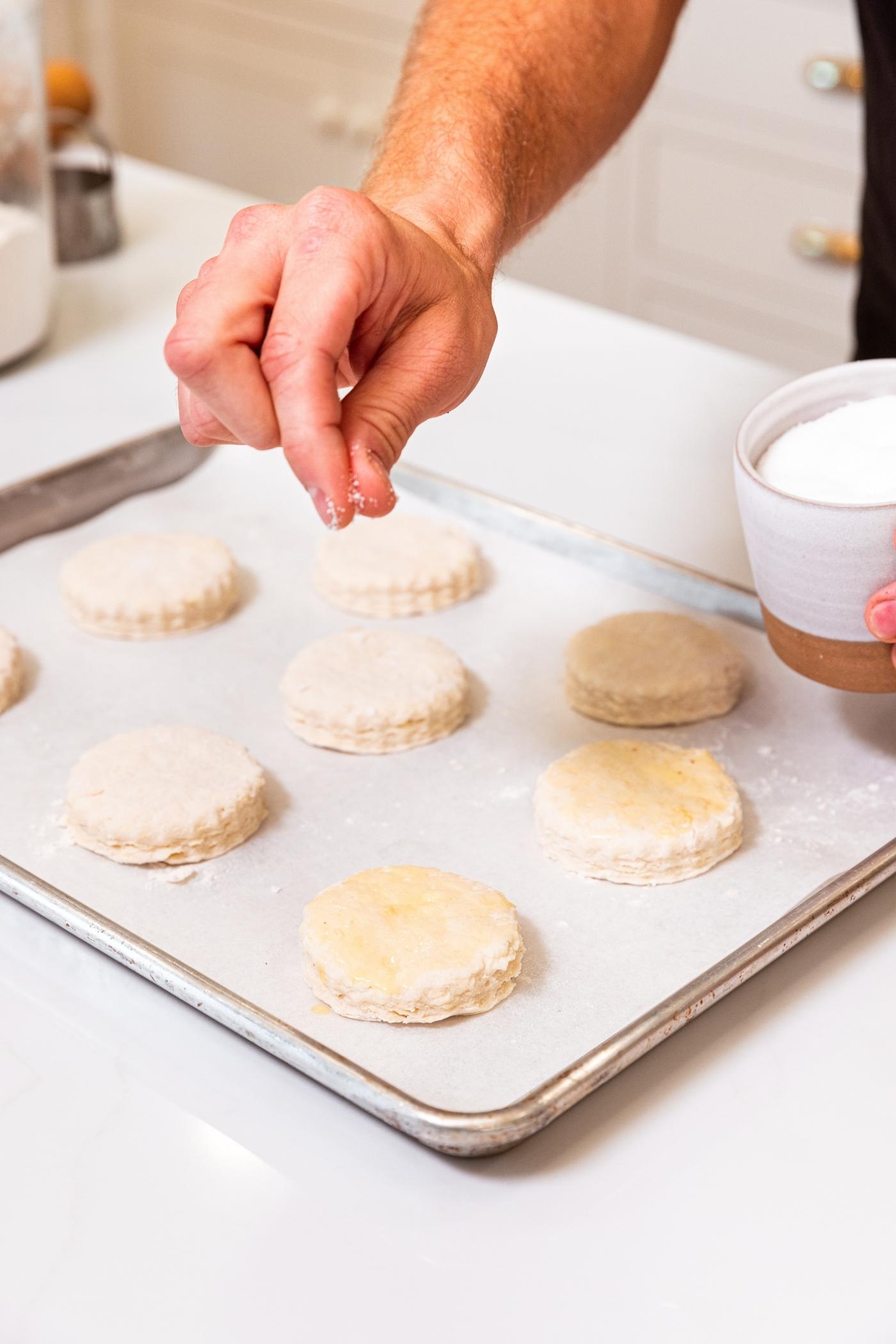 Hand sprinkling salt all over the top of unbaked biscuits on parchment-lined baking sheet.