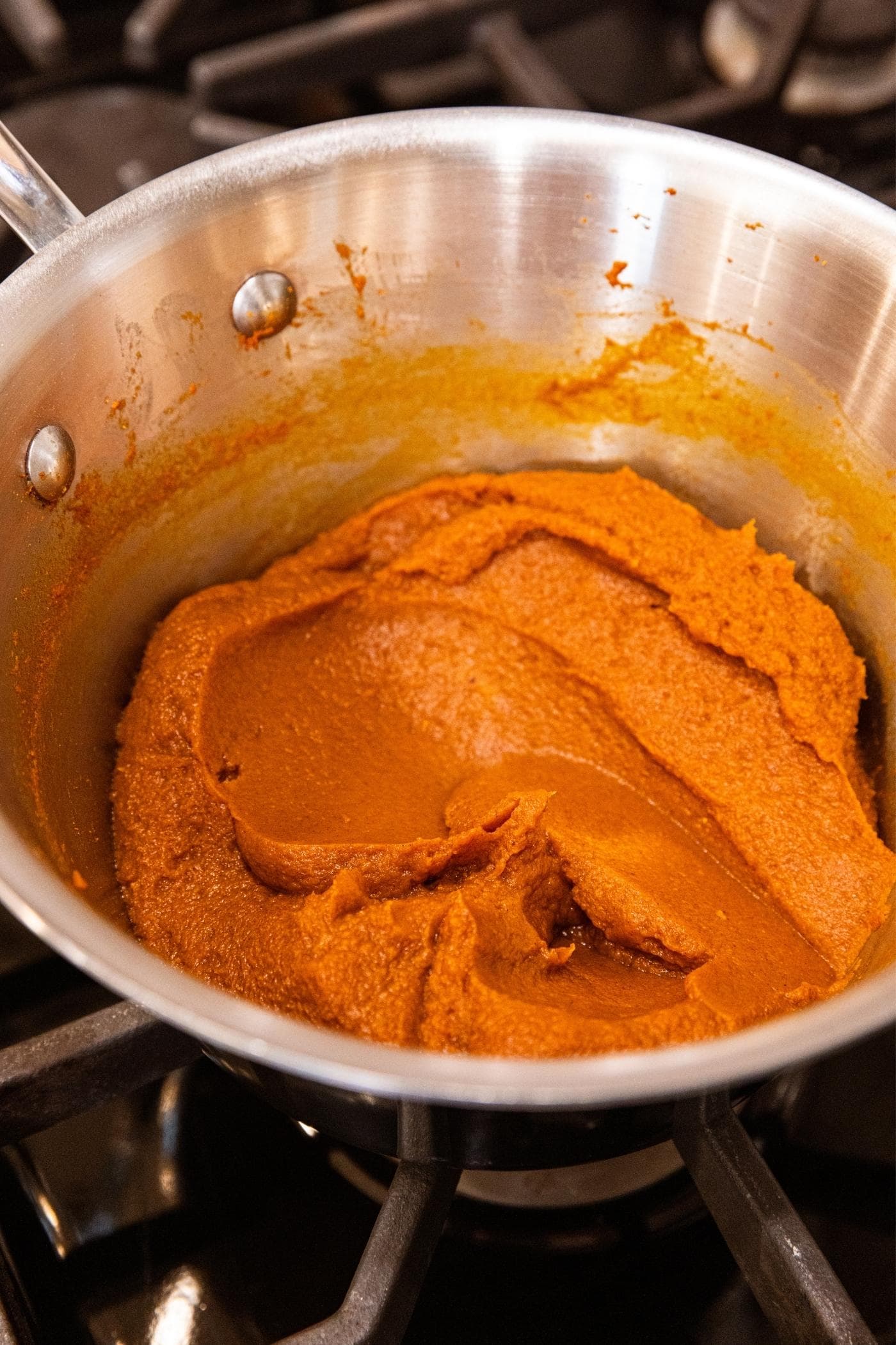 Metal pot sitting on stovetop filled with pumpkin filling after being cooked with heat.
