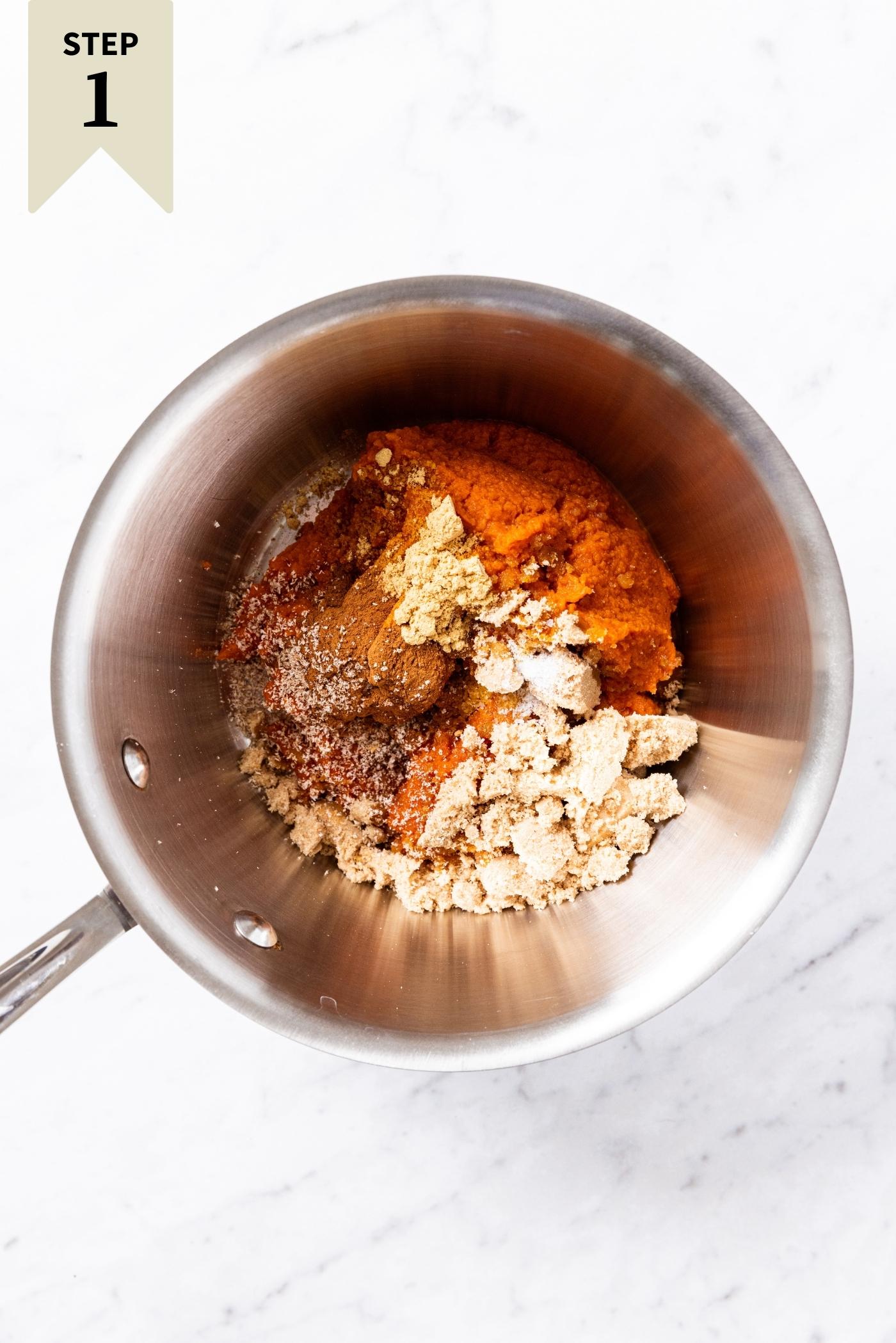 Metal pot sitting on marble surface filled with the ingredients needed to make pumpkin filling including sugar, spices, and pumpkin.