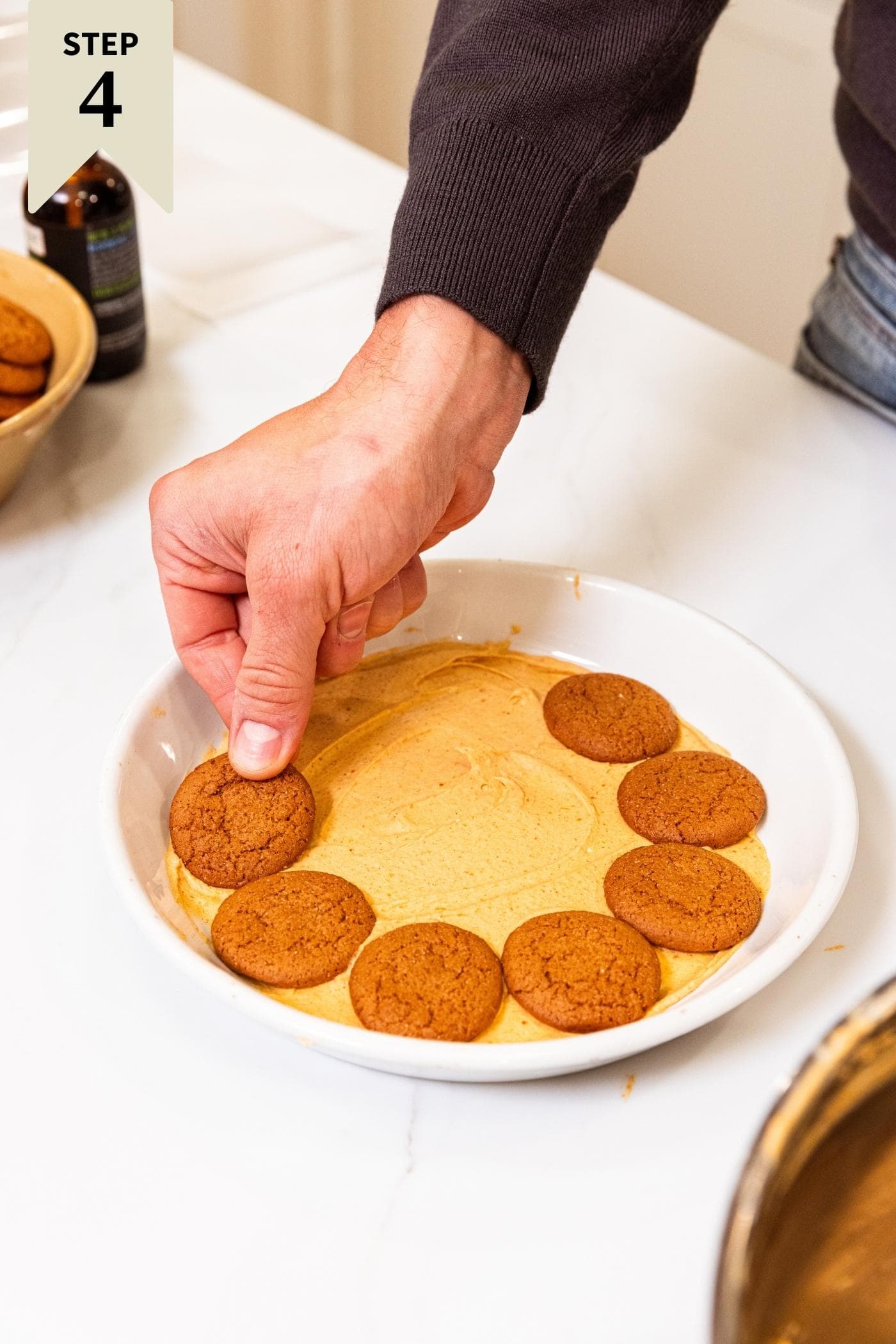 White serving platter filled with pumpkin whipped cream with hand arranging gingersnap cookies on top of filling.
