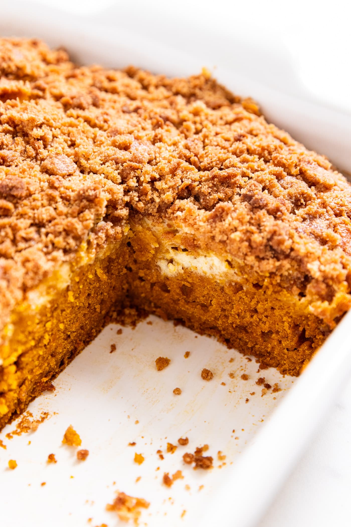 White baking dish with pumpkin coffee cake with cheesecake swirl layer showing sitting in white baking dish.