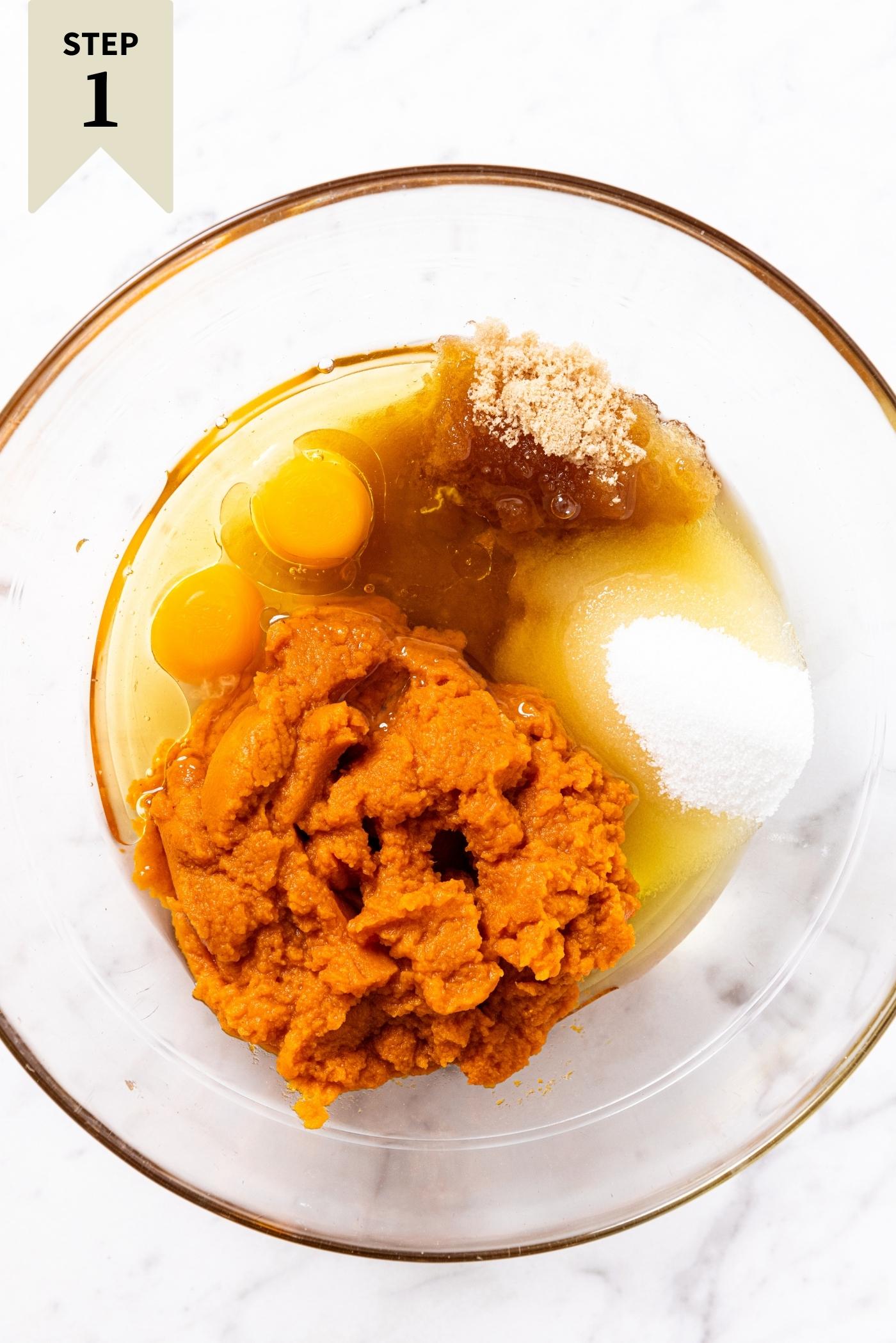 Glass bowl sitting on marble surface filled with pumpkin, eggs, sugar, vanilla extract, and oil before being mixed up into a pumpkin batter.