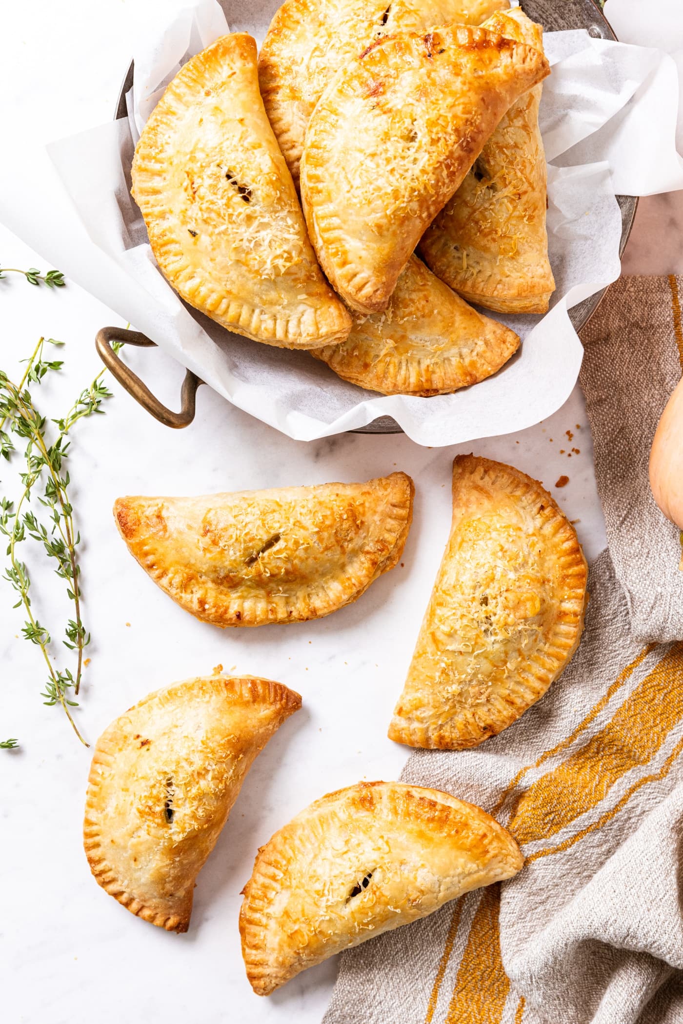 Marble surface filled with lots of baked hand pies that are golden in color with fresh thyme to the side.