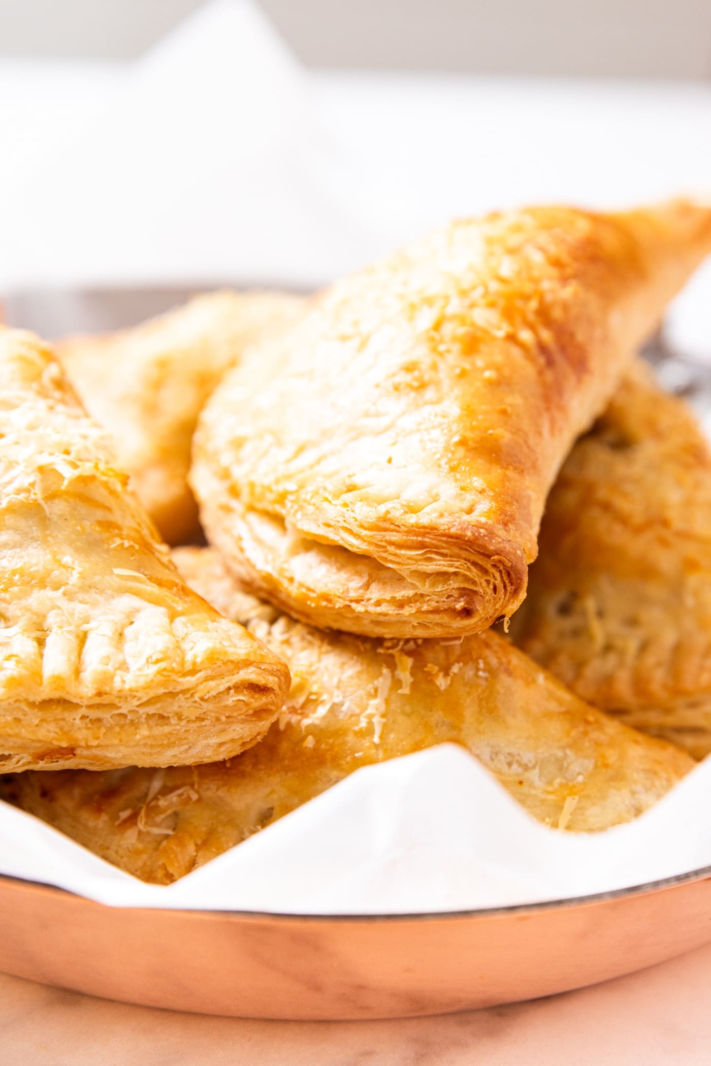 Baked hand pies sitting on top of each other in copper pot sitting on marble surface.