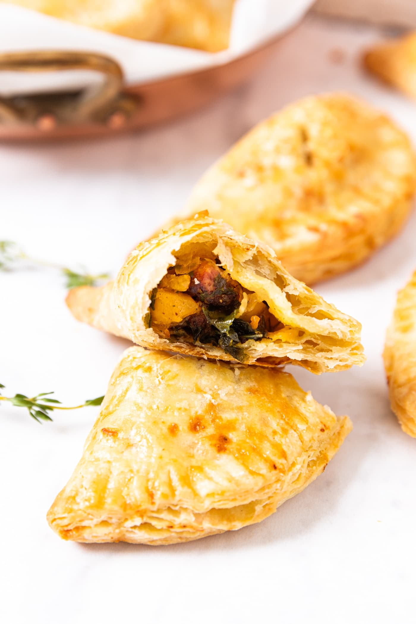Marble surface with baked hand pie cut in half with one half sitting on top of the other showing the inside filled with butternut squash and sausage mixture with more hand pies in background.