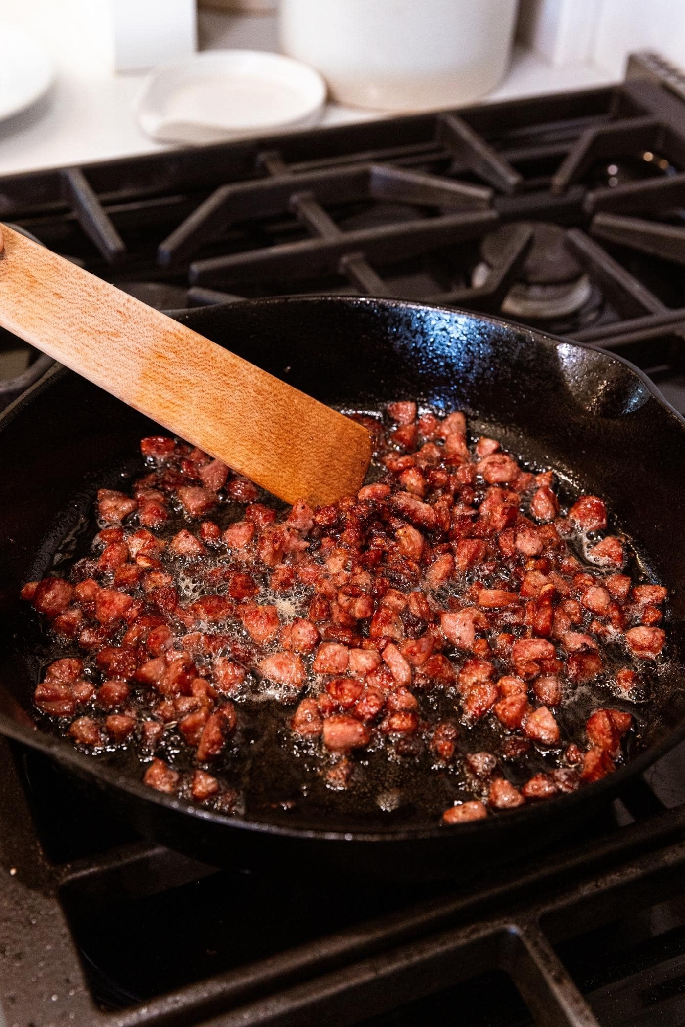 Wooden spatula mixing cooked sausage cut into a small dice in cast iron skillet on stovetop.