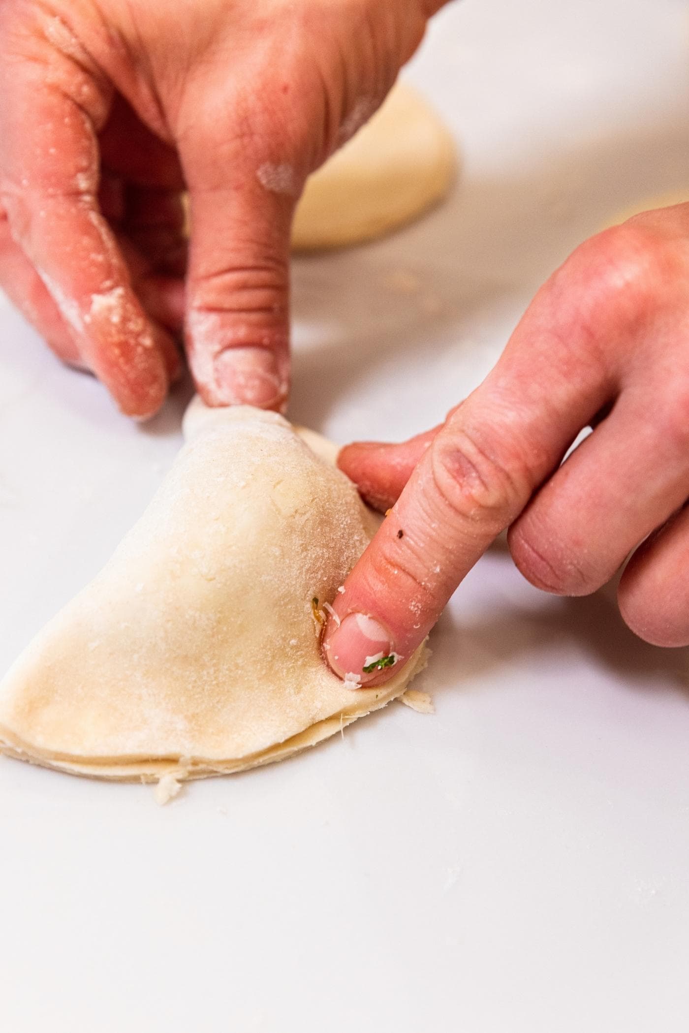 Hand pressing down sides of half moon shaped hand pie filled with butternut squash mixture all on white countertop.