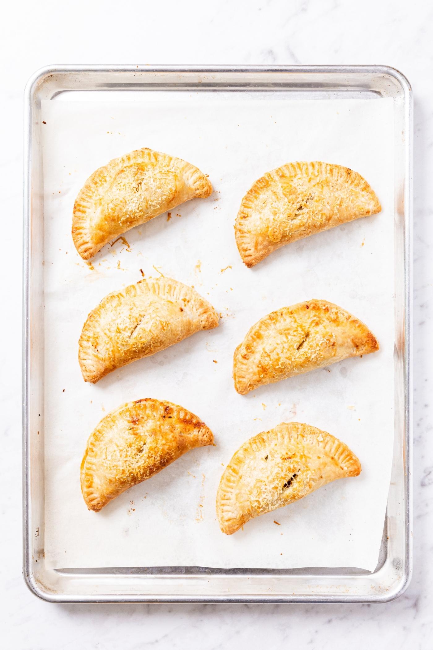 Six hand pies sitting on parchment-lined baking sheet after coming out of oven.