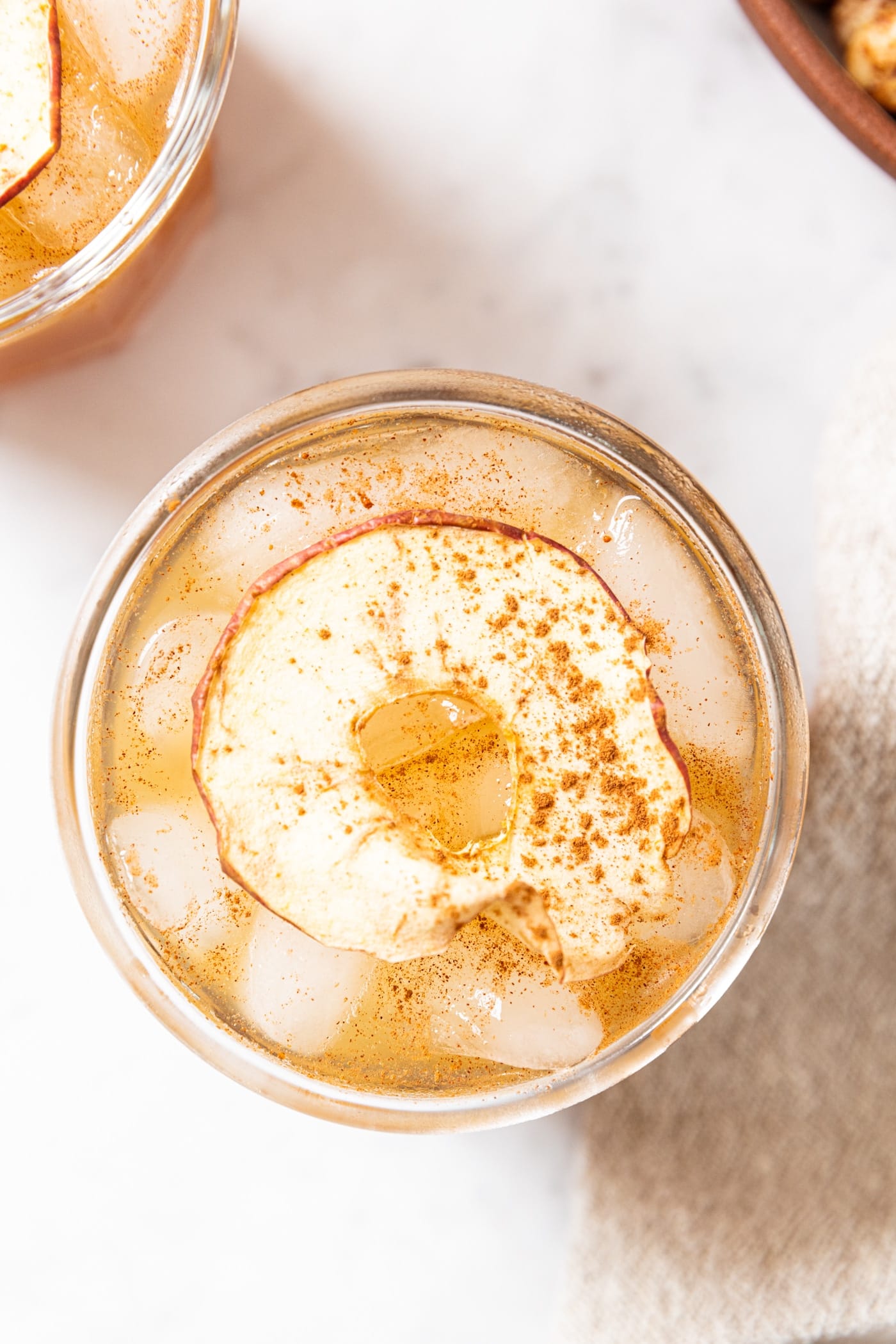 Top of glass filled with spiked apple cider sitting on marble surface with cinnamon sprinkled on top and homemade apple chip slices.