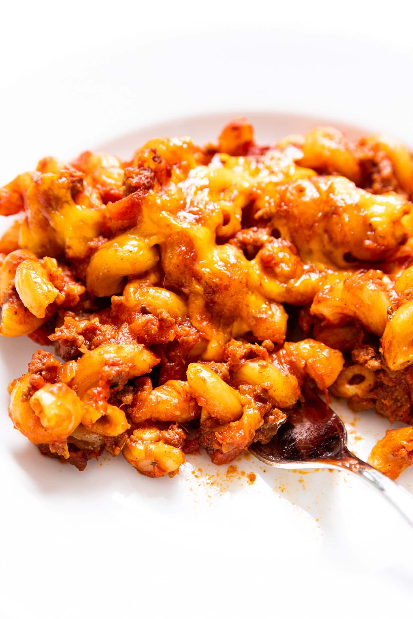 Serving of baked goulash sitting on white plate with fork about to take a bite full of tomato-covered noodles.