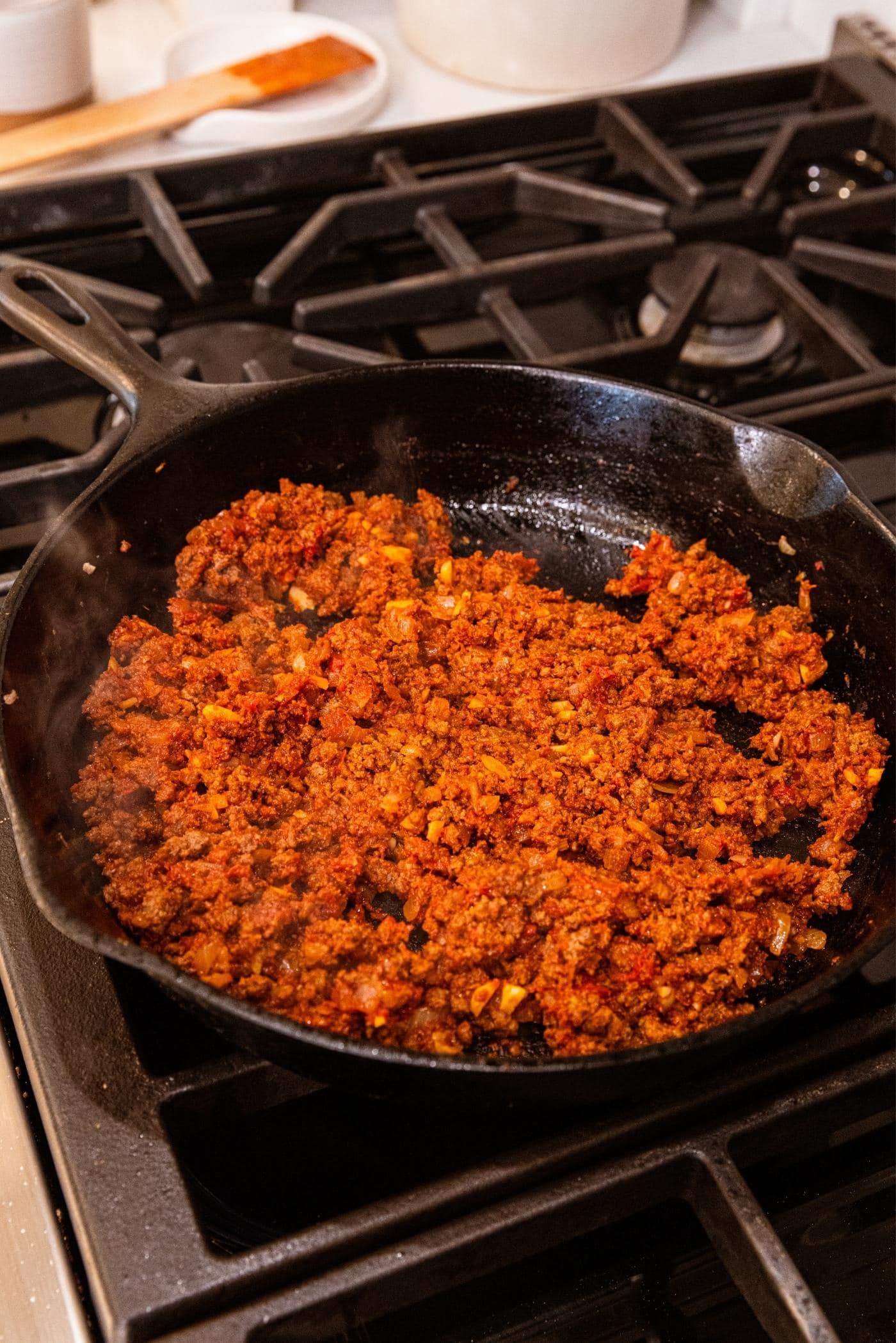 Black cast iron skillet filled with red colored ground beef mixture mixed with tomato paste.