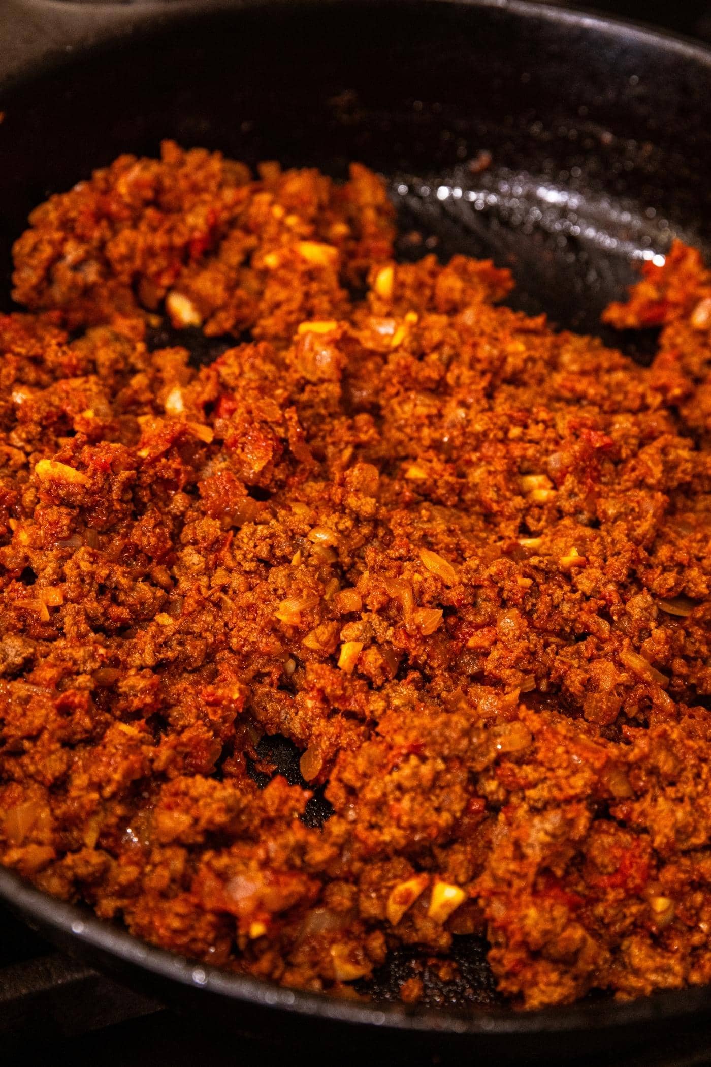 Red colored ground beef mixture sitting in cast iron skillet on stove top after cooking for awhile.