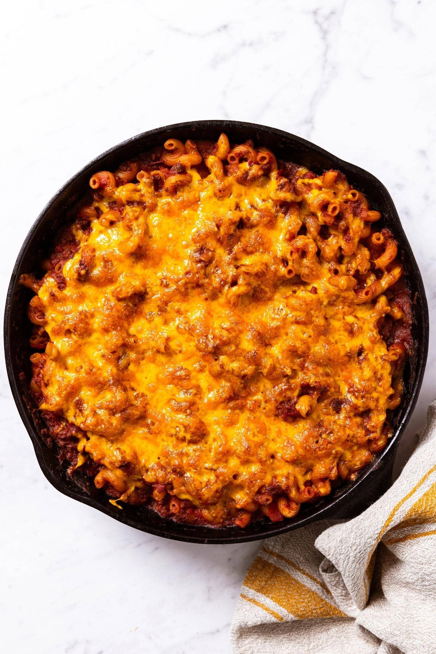 Black cast iron skillet sitting on marble surface after being baked in the oven with melted cheese all over the top. 