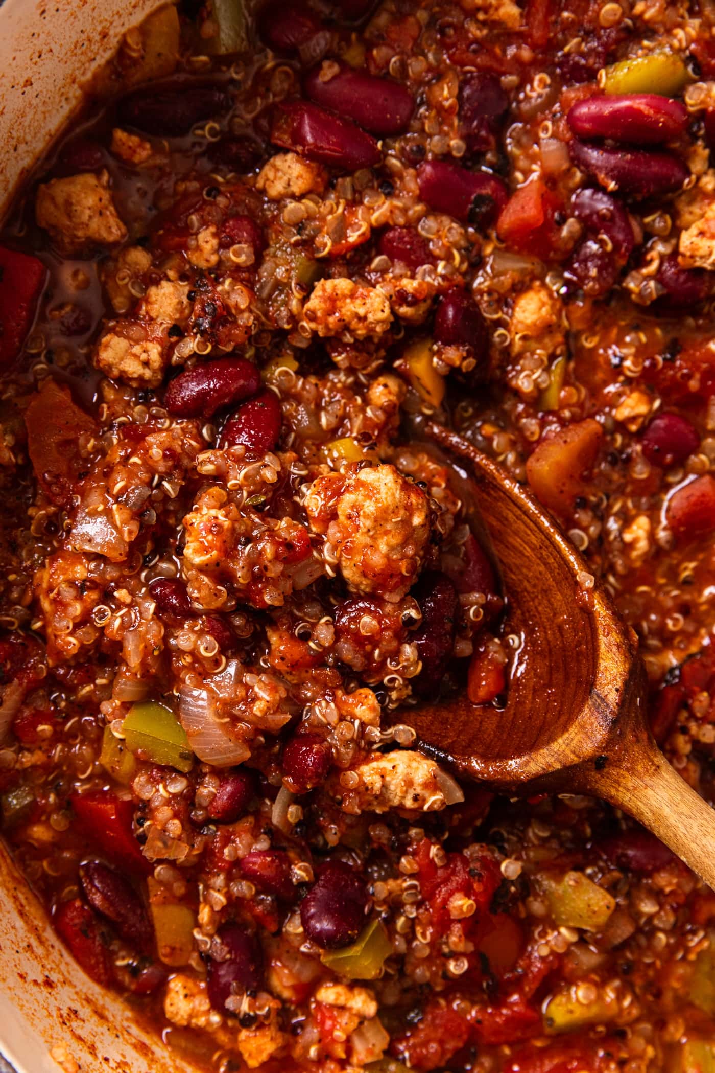 Wooden spoon sitting on top of red colored chili with scoop showing the turkey and beans in the soup.