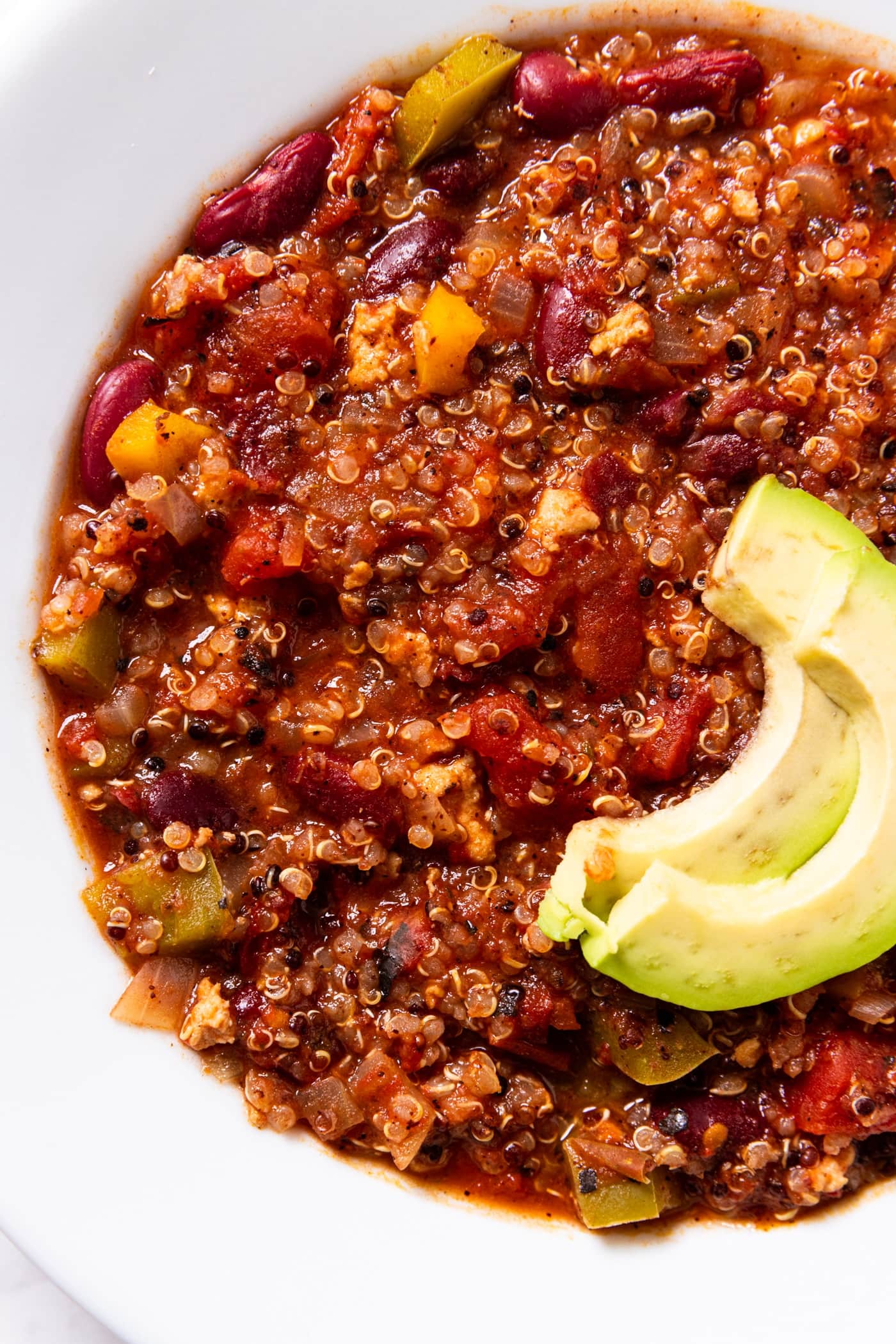 White soup bowl filled with serving of turkey quinoa chili with slices of avocado resting on top.