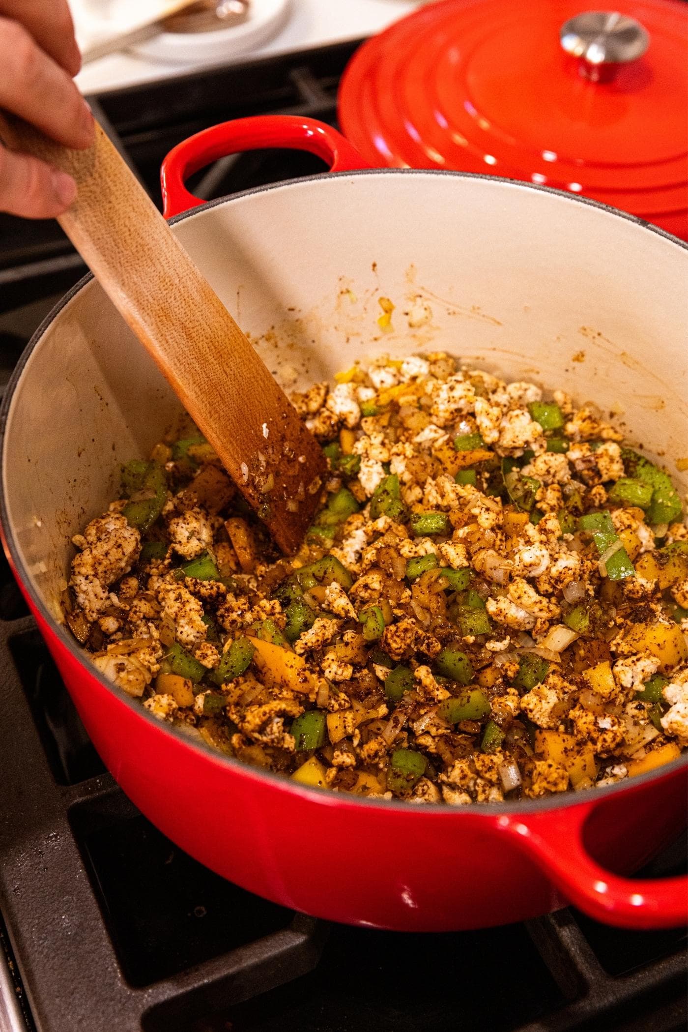 Spices mixed together with ground turkey and onion and bell pepper mixture in red Dutch oven on stovetop with wooden spatula mixing everything together.