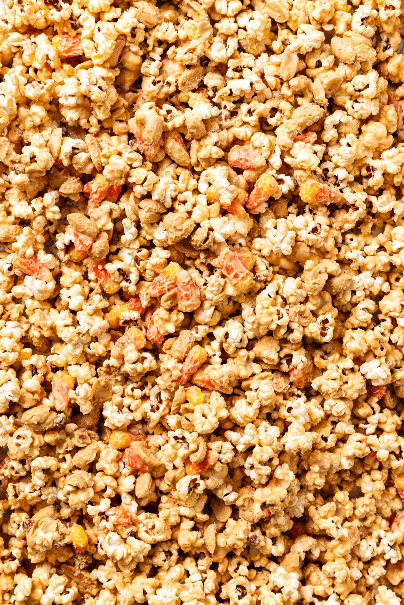 Baking sheet filled with peanut butter covered popcorn with pieces of candy corn and peanuts mixed in.