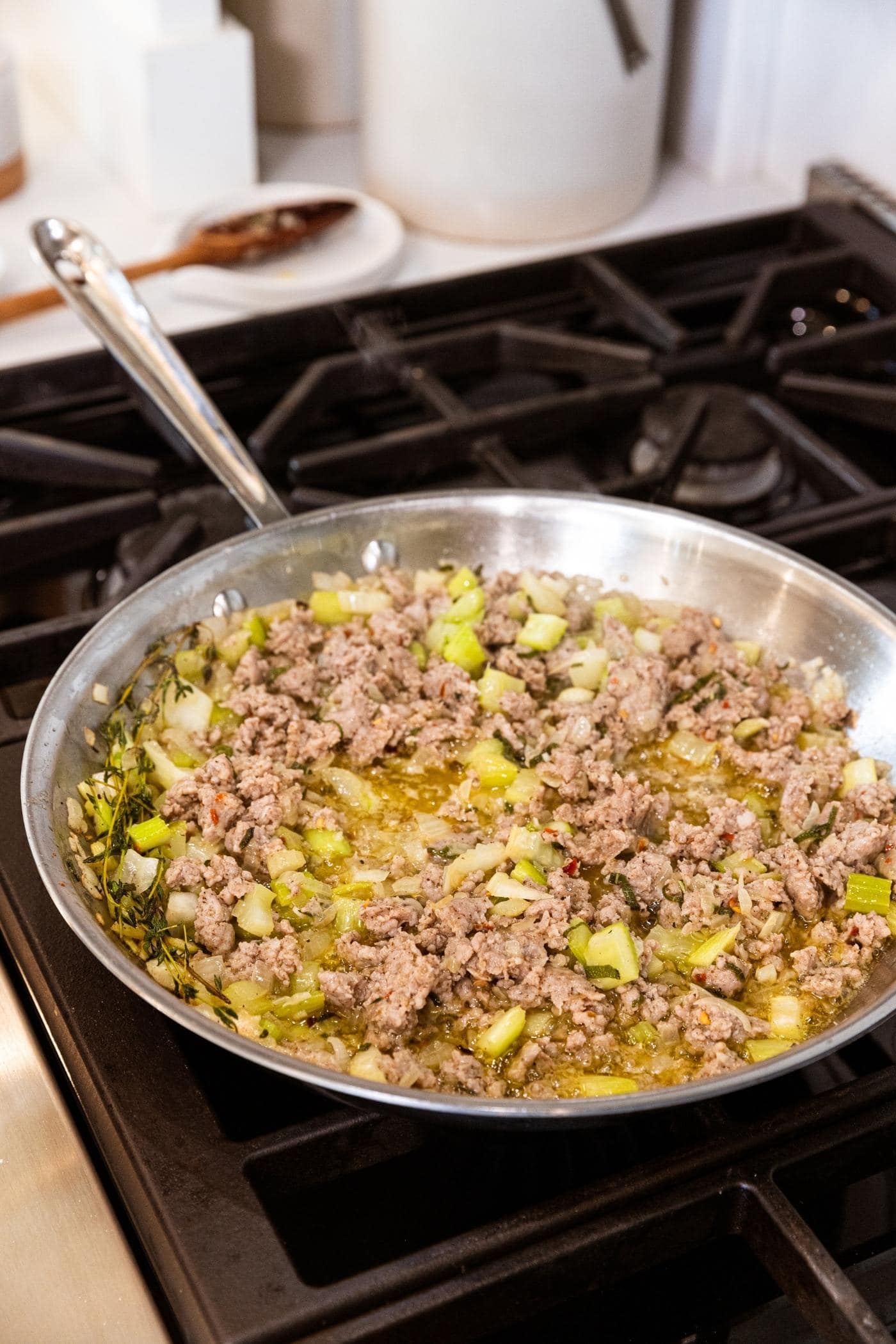 Browned ground sausage sitting in melted butter with pieces of diced onion and celery sitting as well in skillet on stovetop.