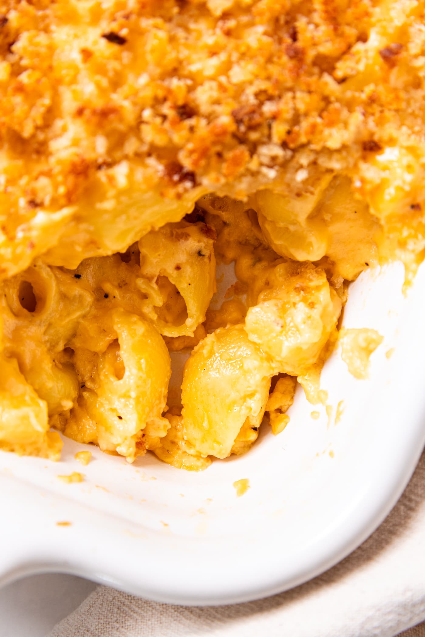 Baked macaroni & cheese sitting in white baking dish showing the elbow macaroni pasta covered with cheese and breadcrumb topping.