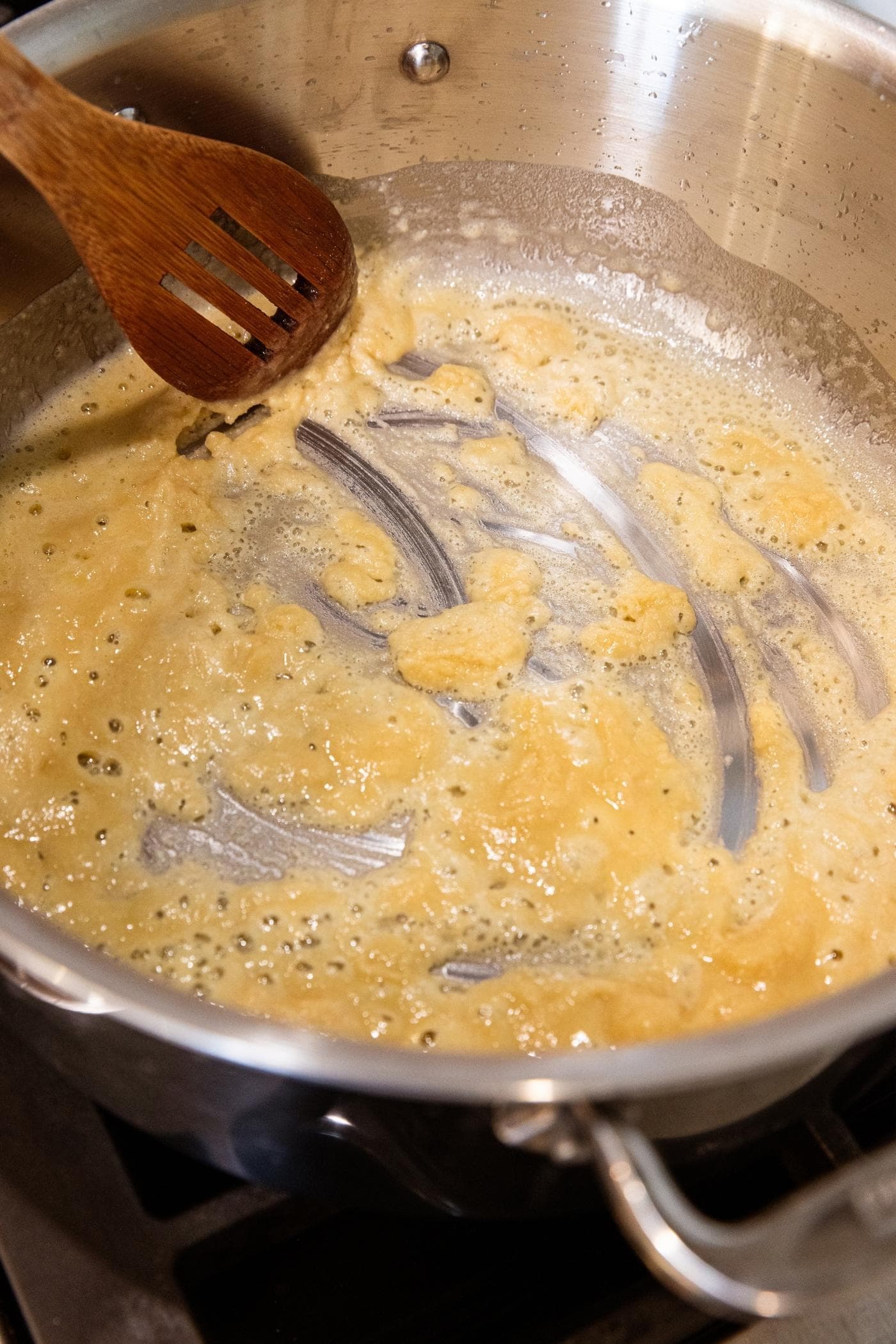 Brown colored roux being stirred together in large stockpot on stovetop with wooden spoon stirring everything together.