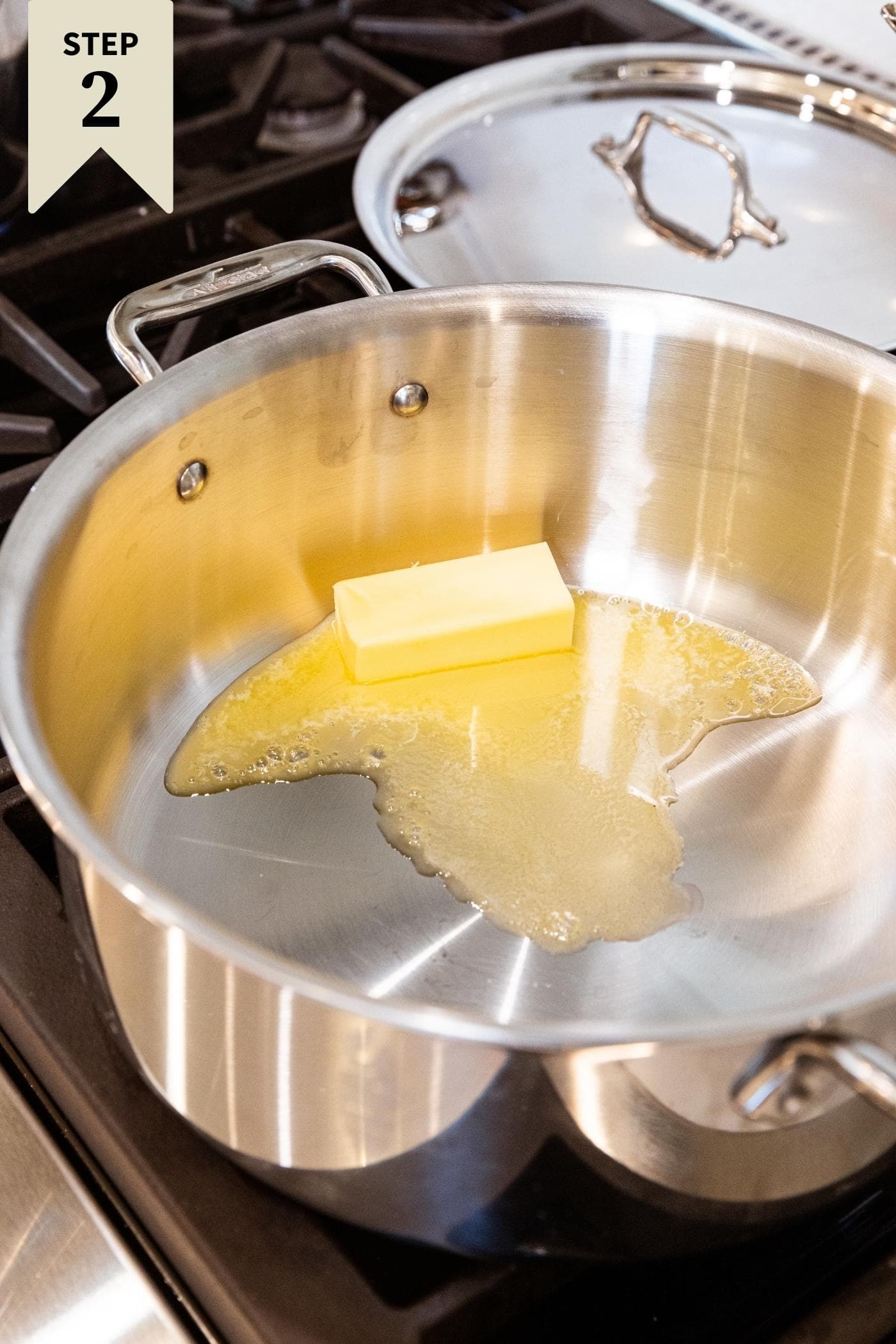 Metal stockpot sitting on stovetop with butter melting and about halfway gone.