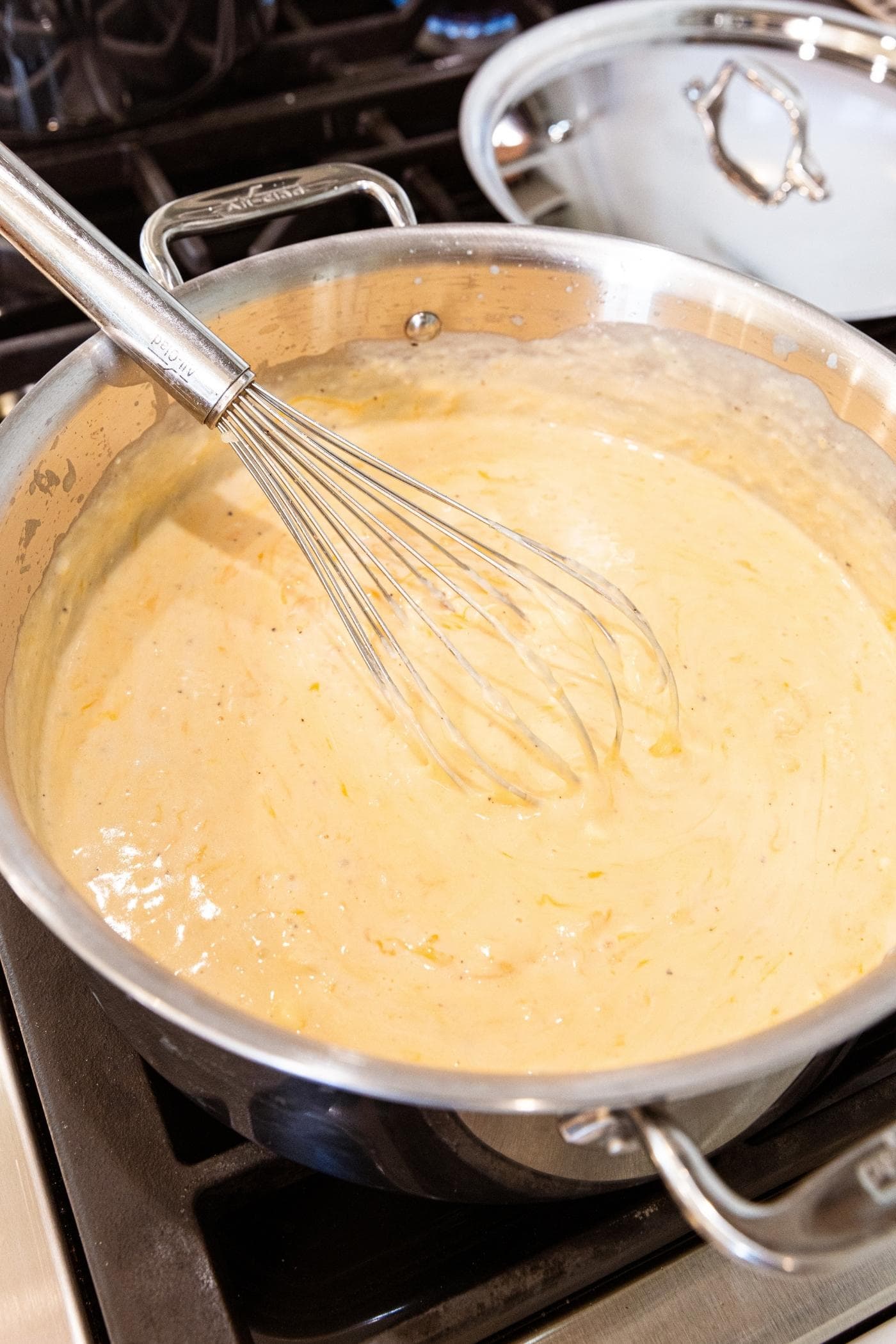 Cheesy milk mixture sitting in metal stockpot with whisk resting against side of pot.