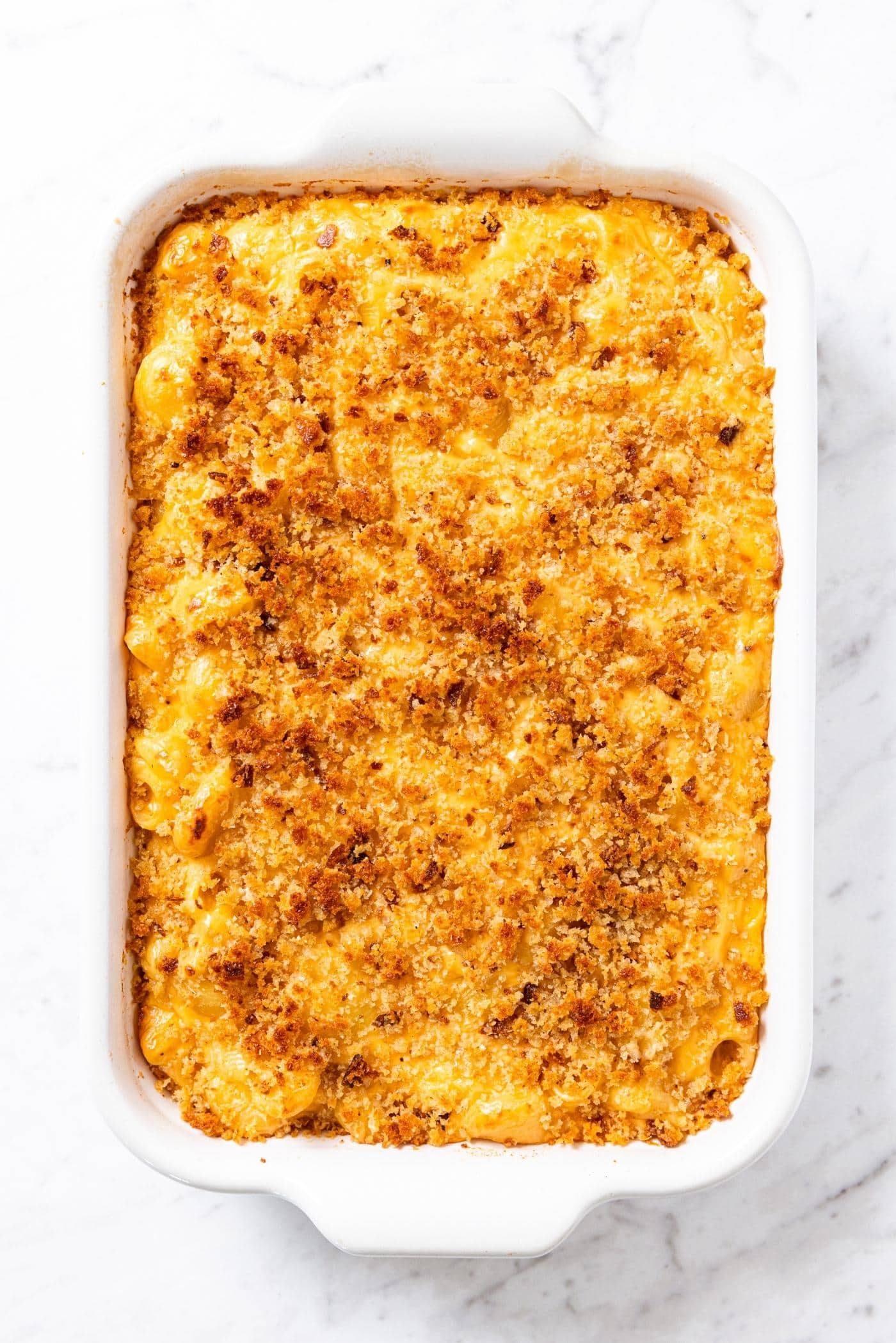 Baked macaroni & cheese mixture in white baking dish with browned topping after coming out of the oven.