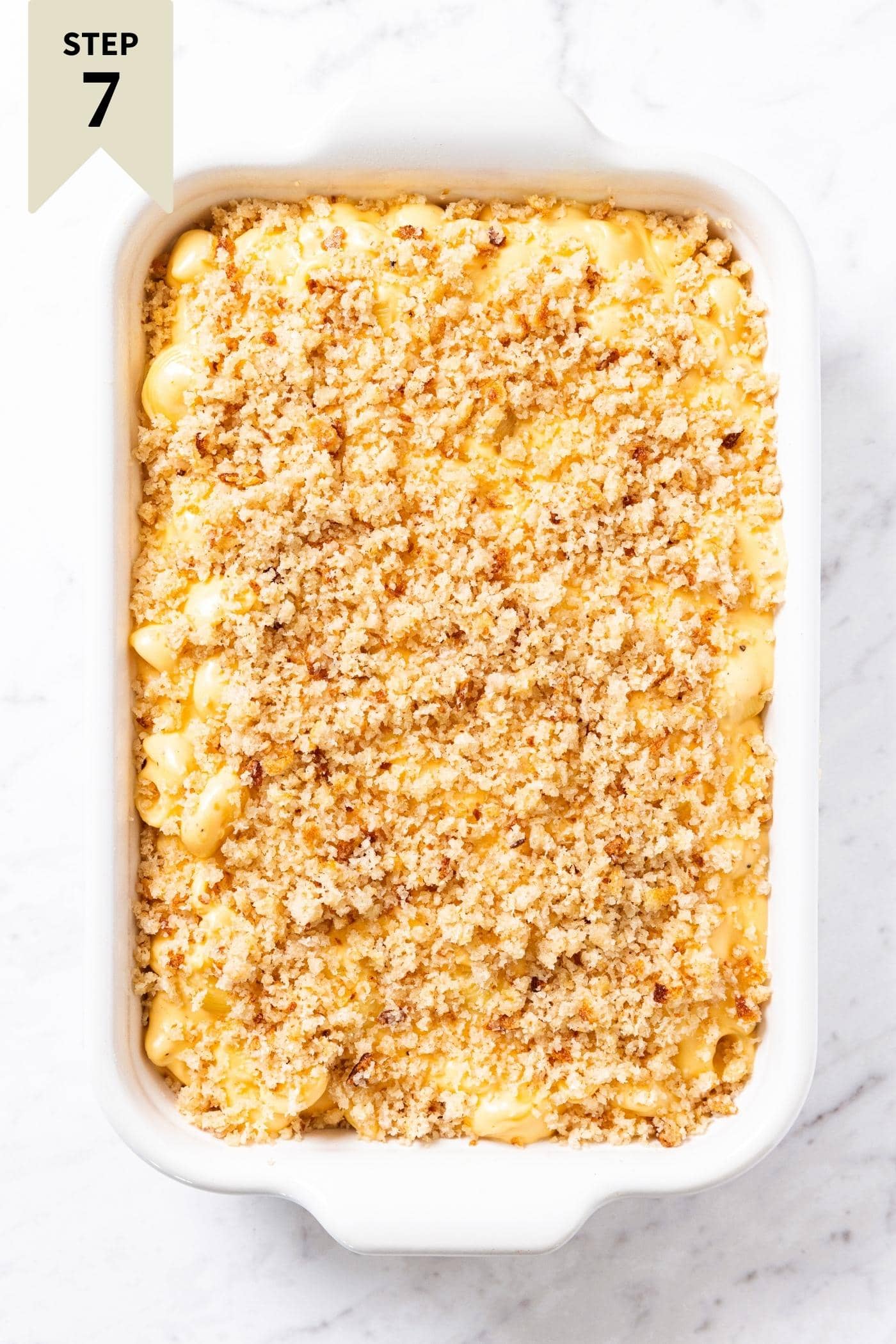 Unbaked macaroni & cheese with breadcrumb topping sitting on marble surface right before being put in the oven to bake.