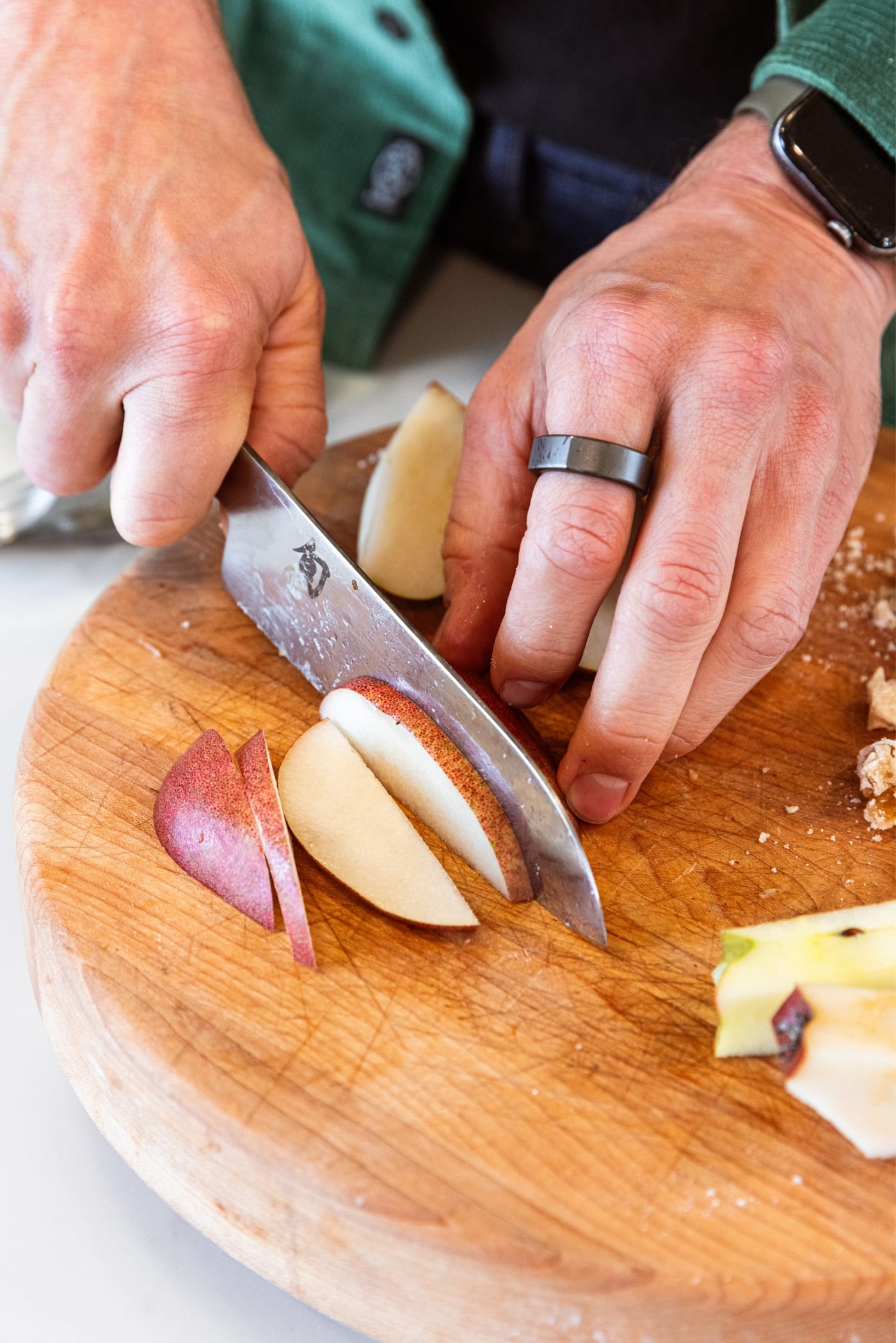 Hand using knife to slice pear into thin slices on a wooden cutting board.