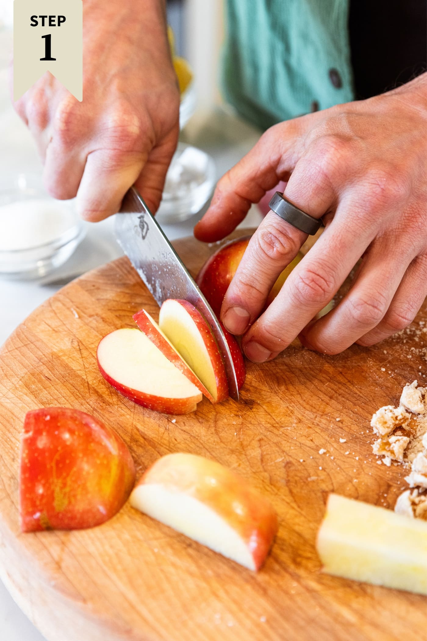 Hand using knife to slice an apple into thin slices on a wooden cutting board.
